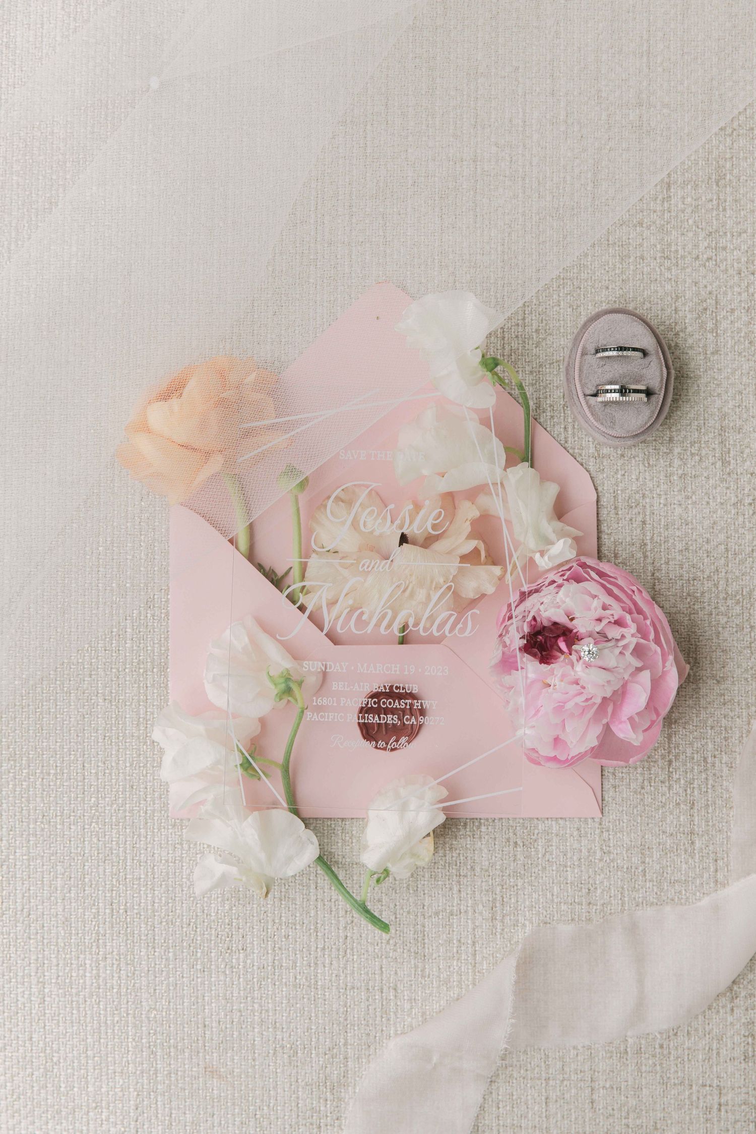 Soft pink and white floral arrangement with ribbons laid on light textured surface.