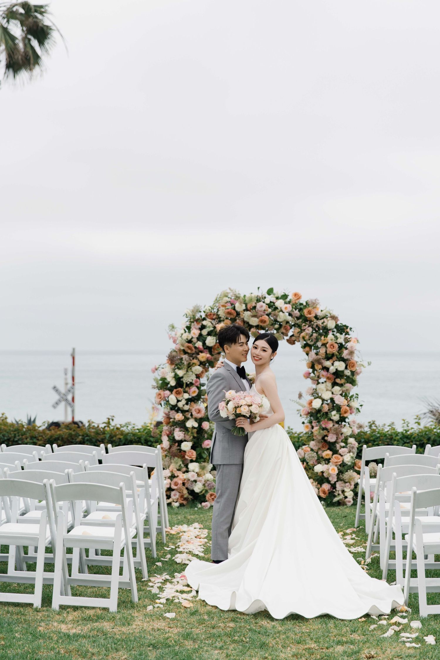 Elegant wedding ceremony with floral arch and white chairs overlooking the ocean.