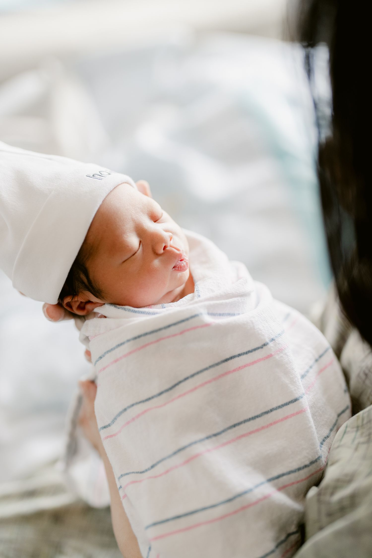 Close-up of sleeping newborn in striped hospital blanket showing tiny features.
