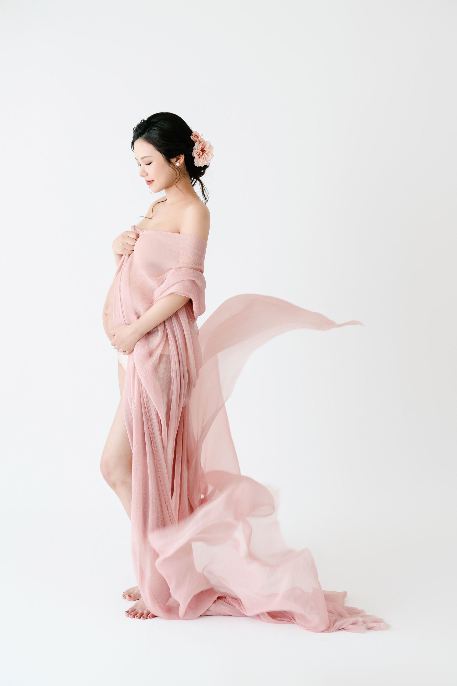 Ethereal maternity photo with flowing pink fabric in studio setting.