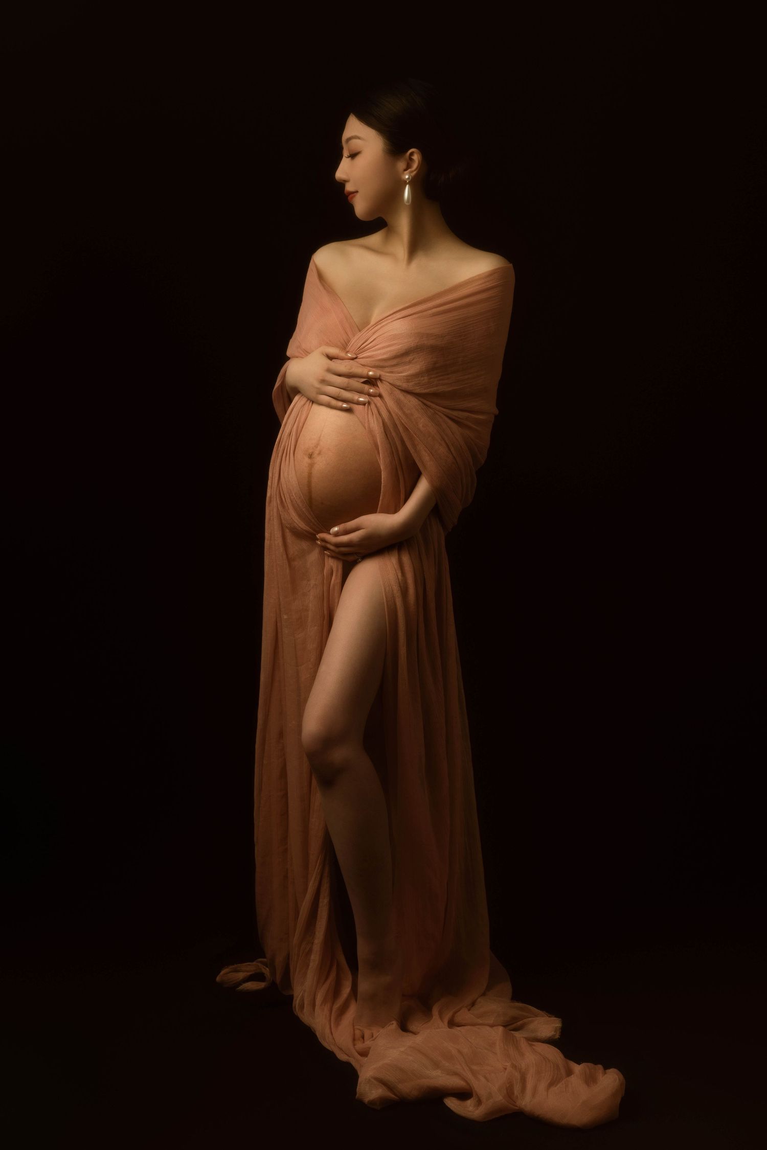 Low-key maternity photography featuring draped mauve fabric against black background.