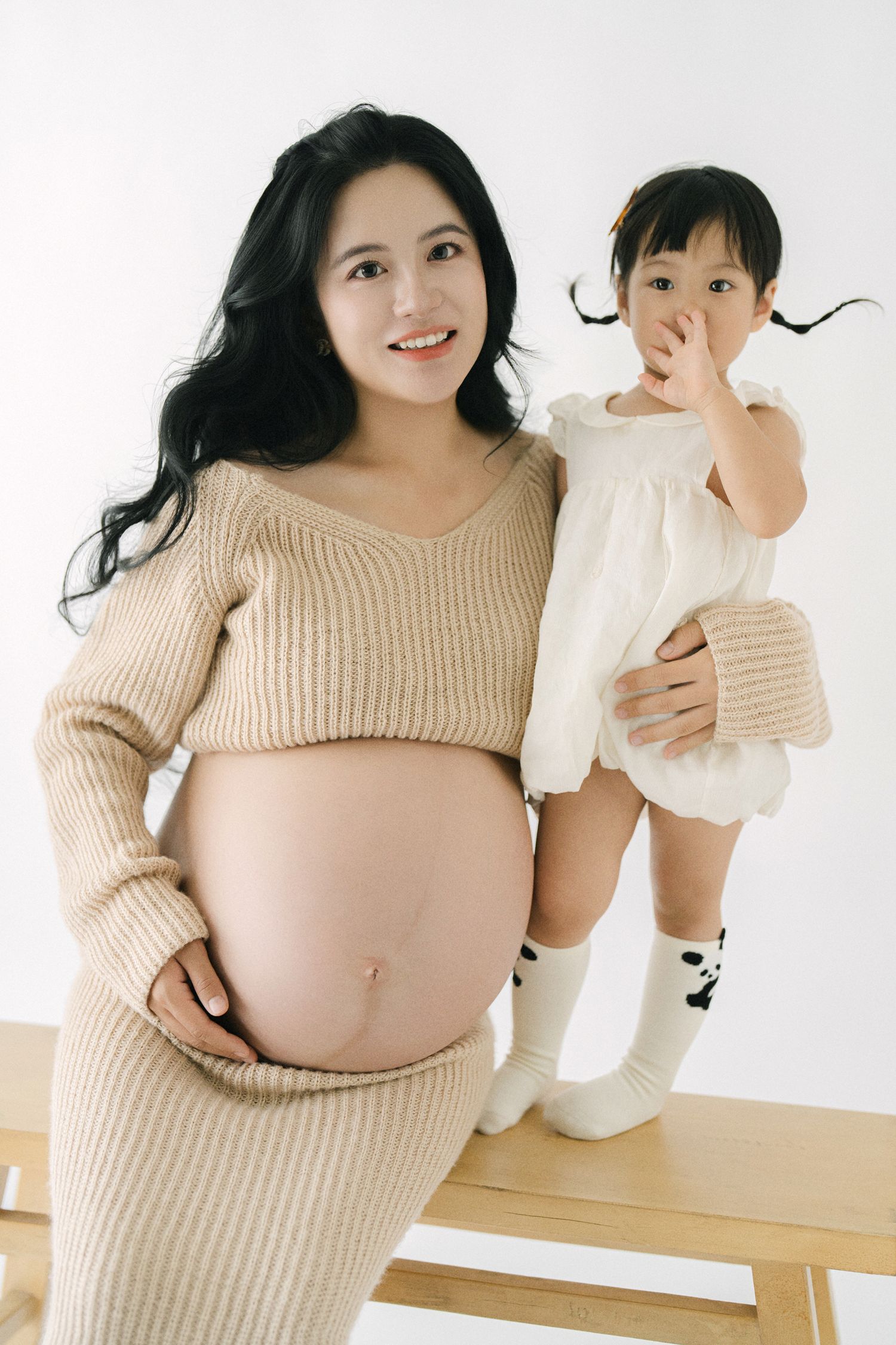 A series of maternity photos showing a woman in beige sweater with her young child in white.