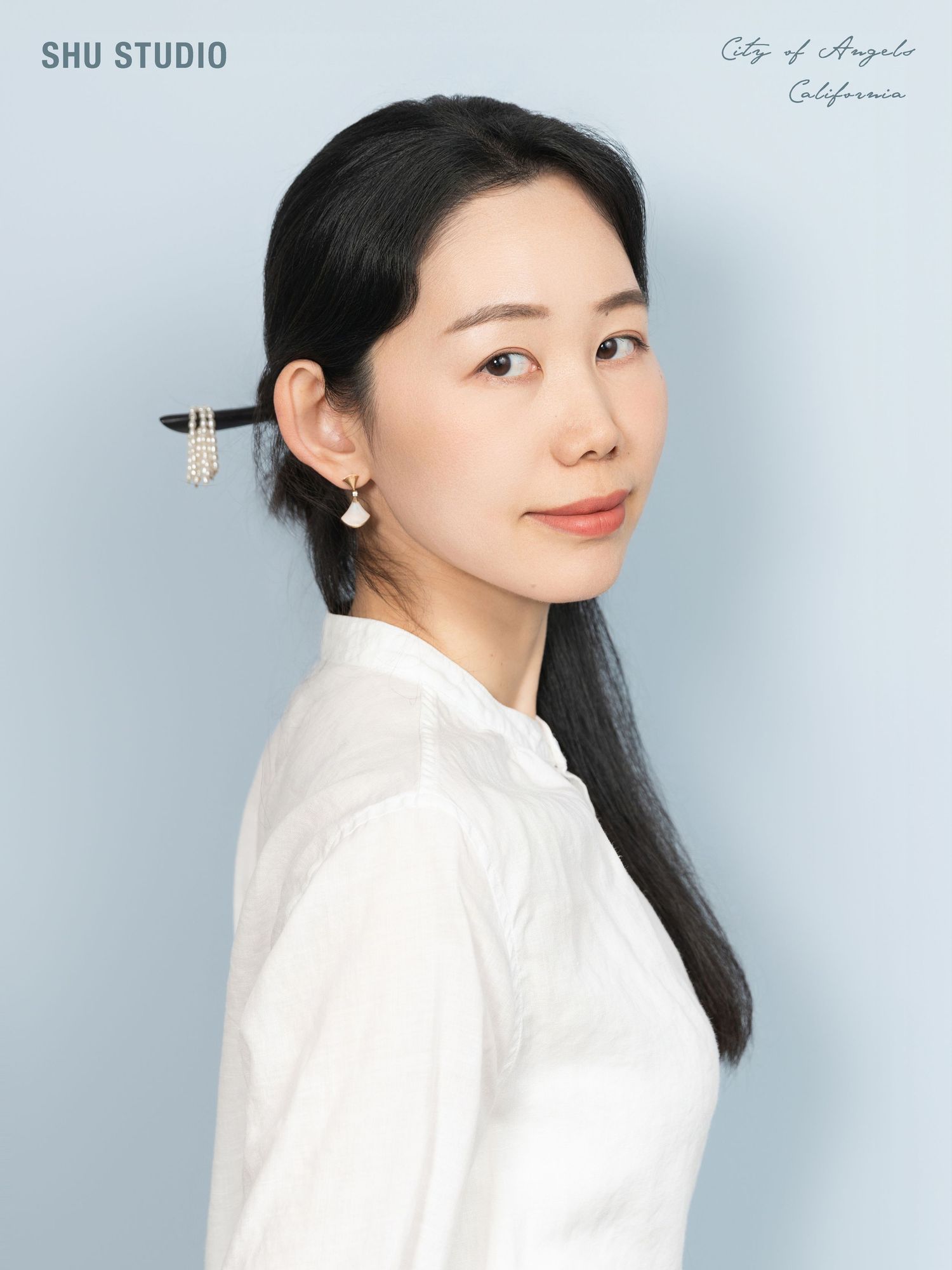 Professional studio portrait with white button-up shirt against light blue background.
