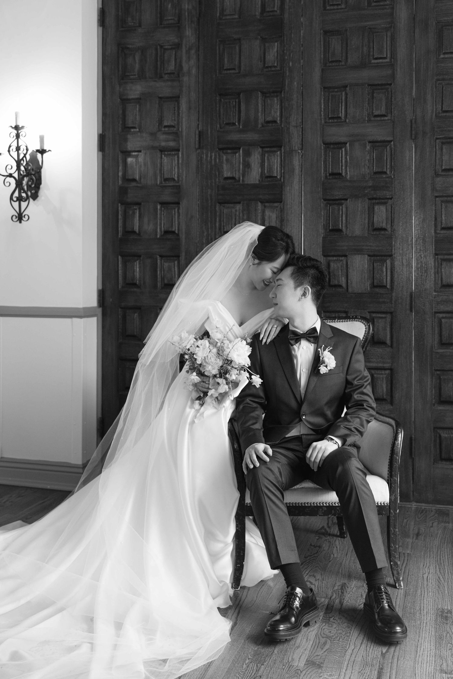Black and white photo of a couple in wedding attire posing dramatically in an elegant room.