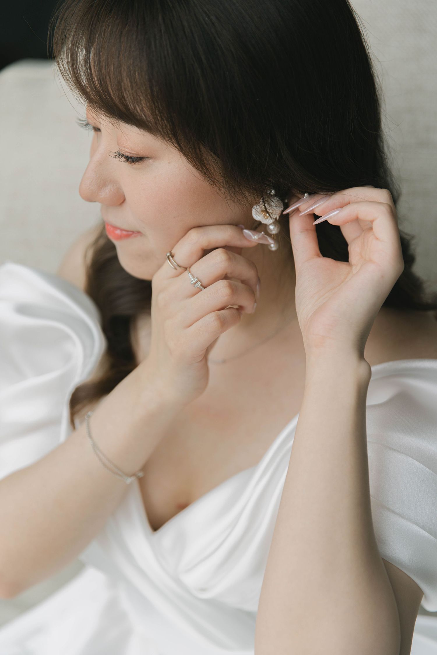 Close-up shots of someone putting on delicate pearl earrings against a light background.