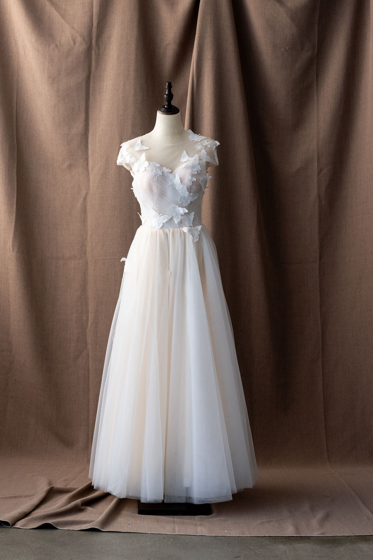 Full-length white tulle wedding dress with empire waist and floral details shown on dress form.