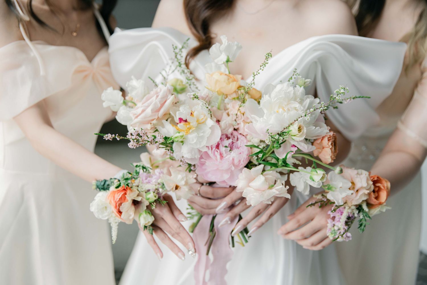 Row of delicate pastel wedding bouquets with pink and white flowers held by hands.