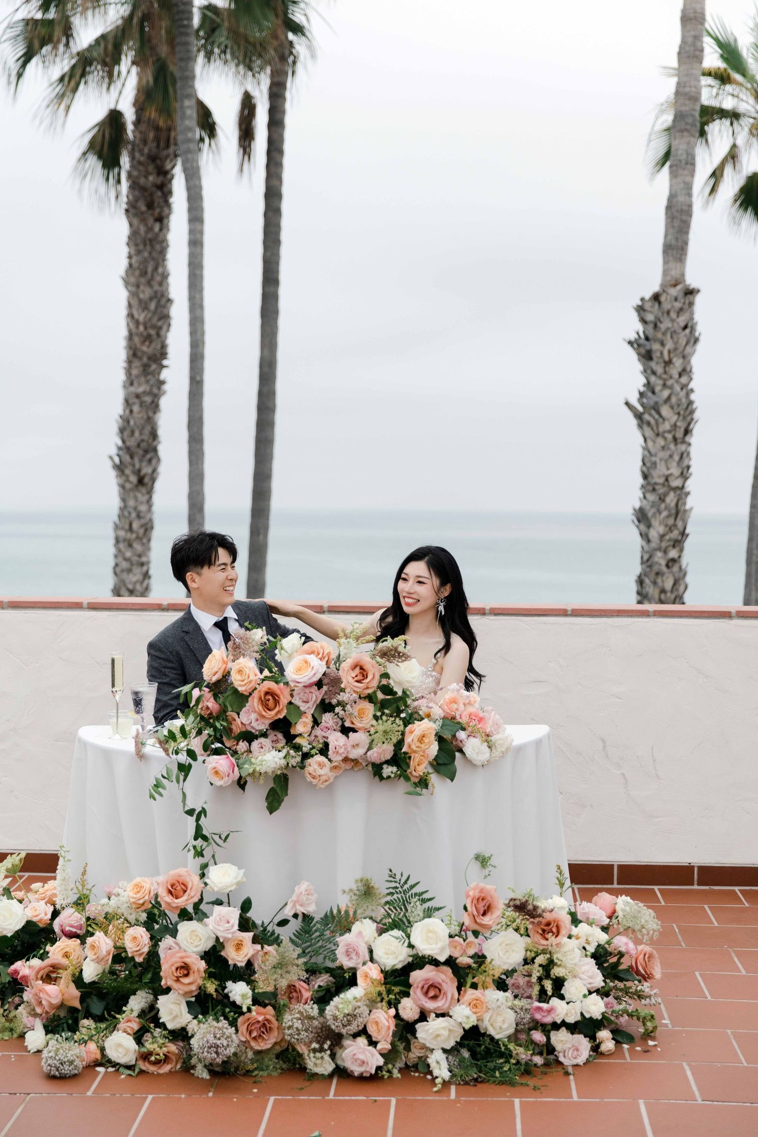 Romantic wedding setup with peach and white floral arrangements along a terrace overlooking the ocean.