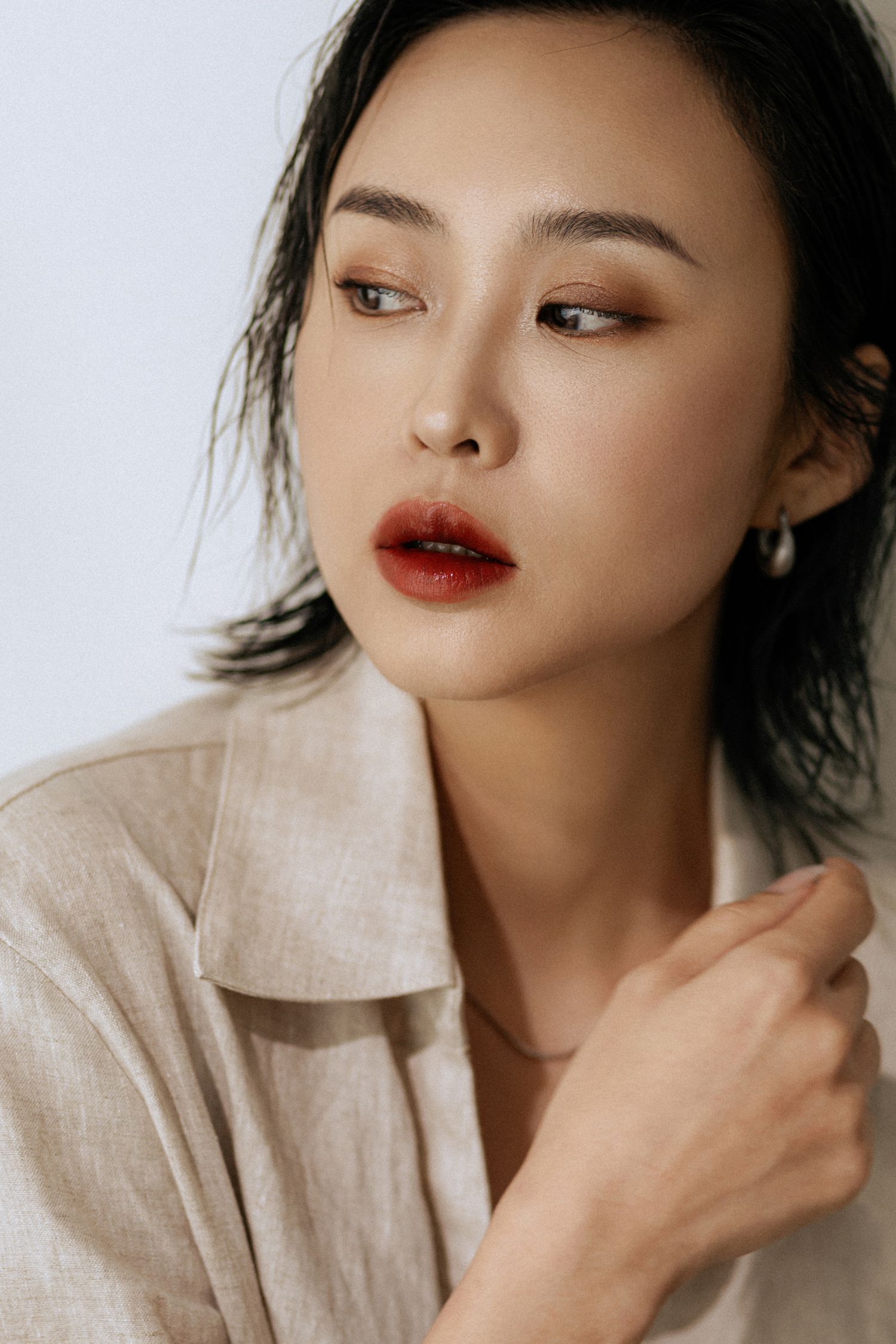 Modern beauty portrait with dewy skin and red lips against white background.