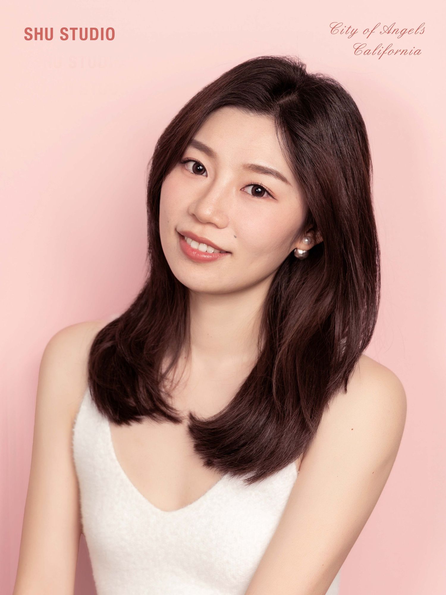 Studio portrait in white sleeveless top against pink background.
