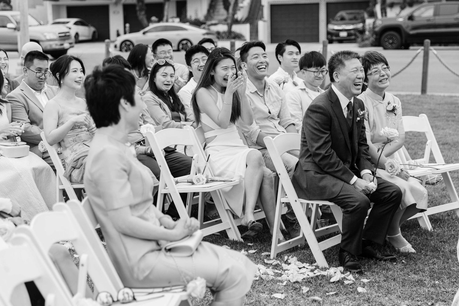 Black and white photo of wedding guests seated on white chairs outdoors.