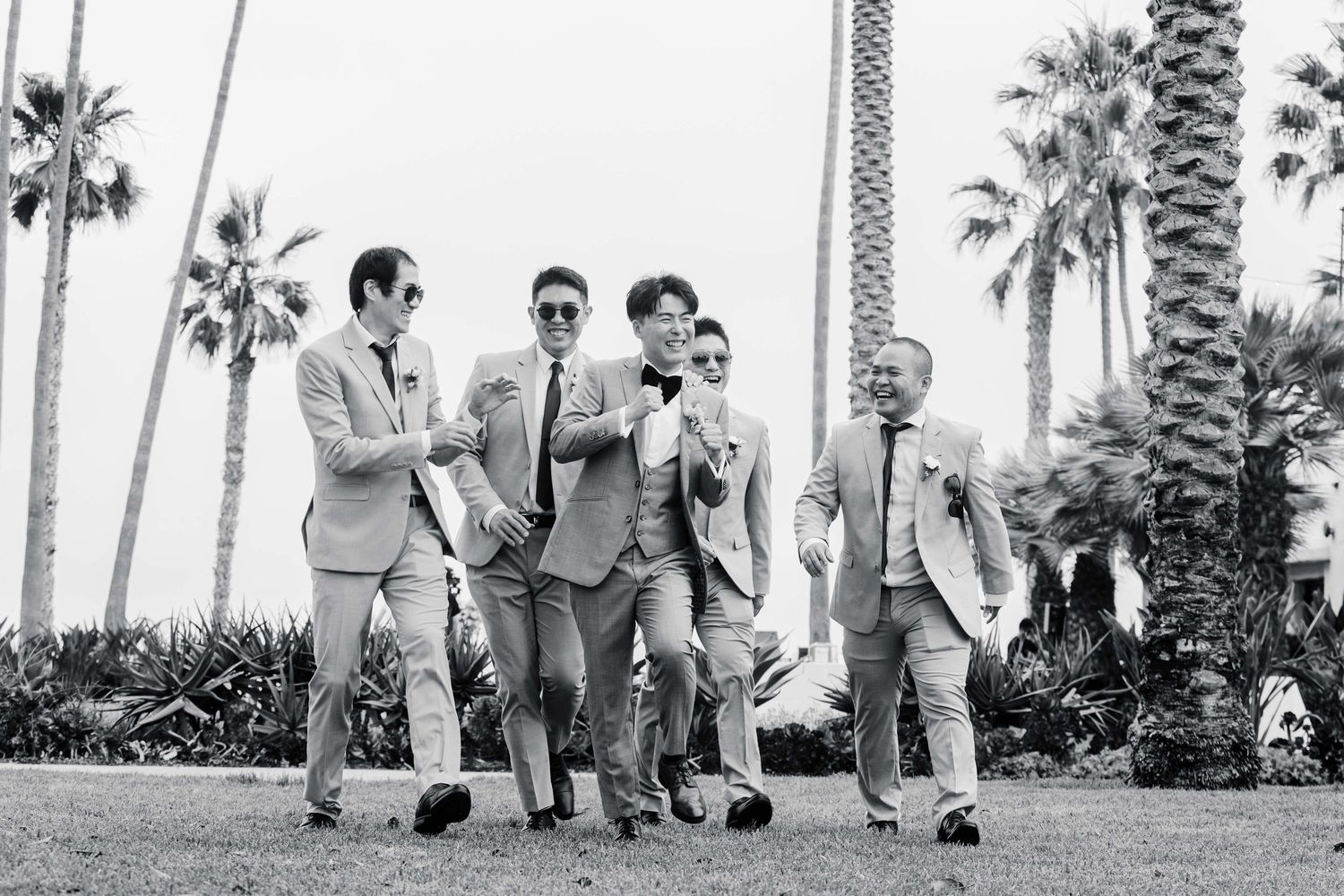 Group of groomsmen walking and laughing together under palm trees.