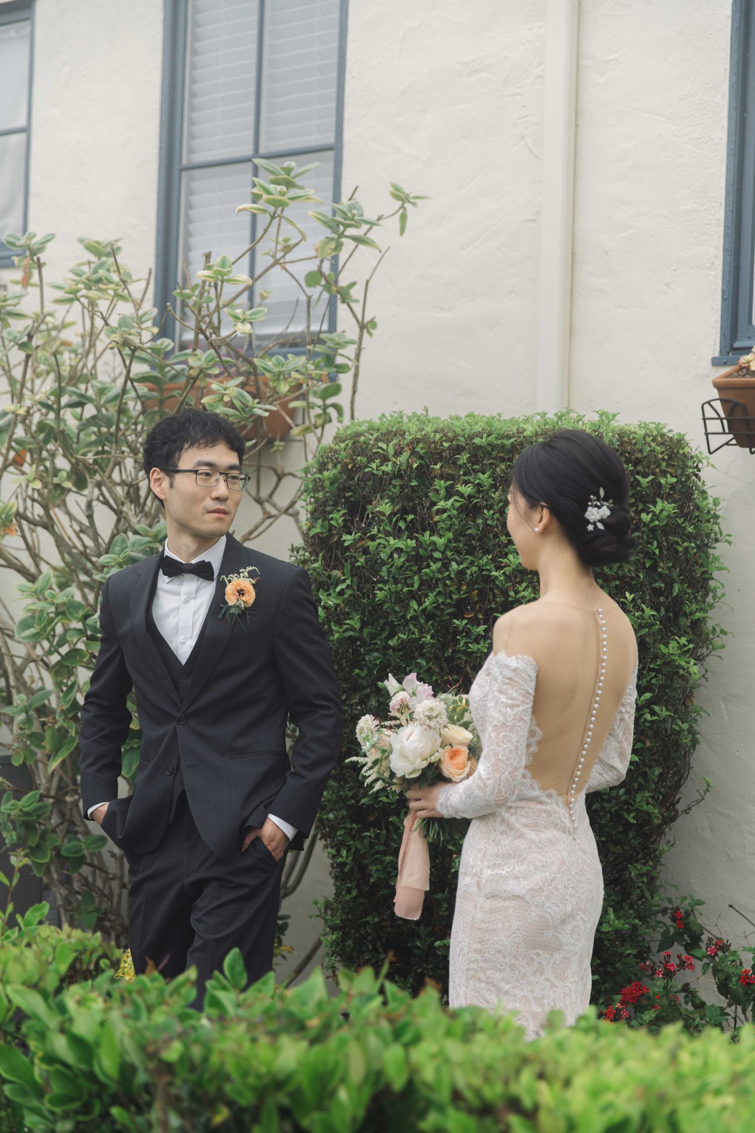 A romantic garden wedding scene with couple sharing a moment among green hedges and white walls.
