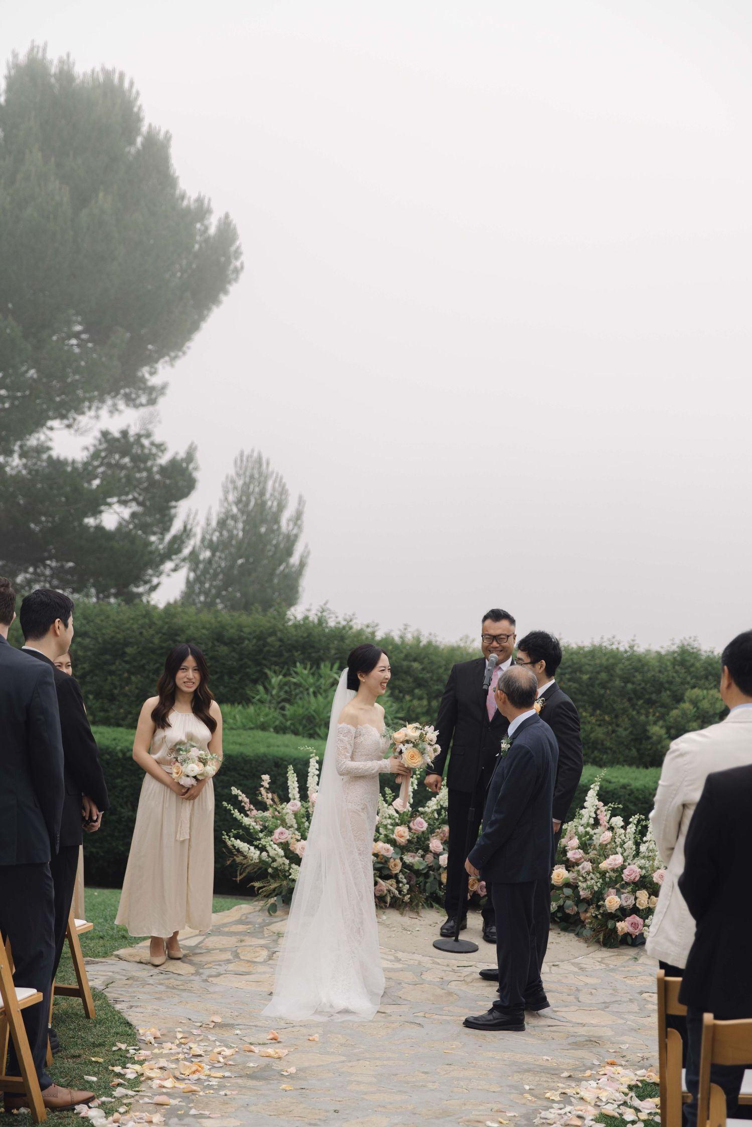 Wedding guests and wedding party gather on a stone patio during an outdoor ceremony.