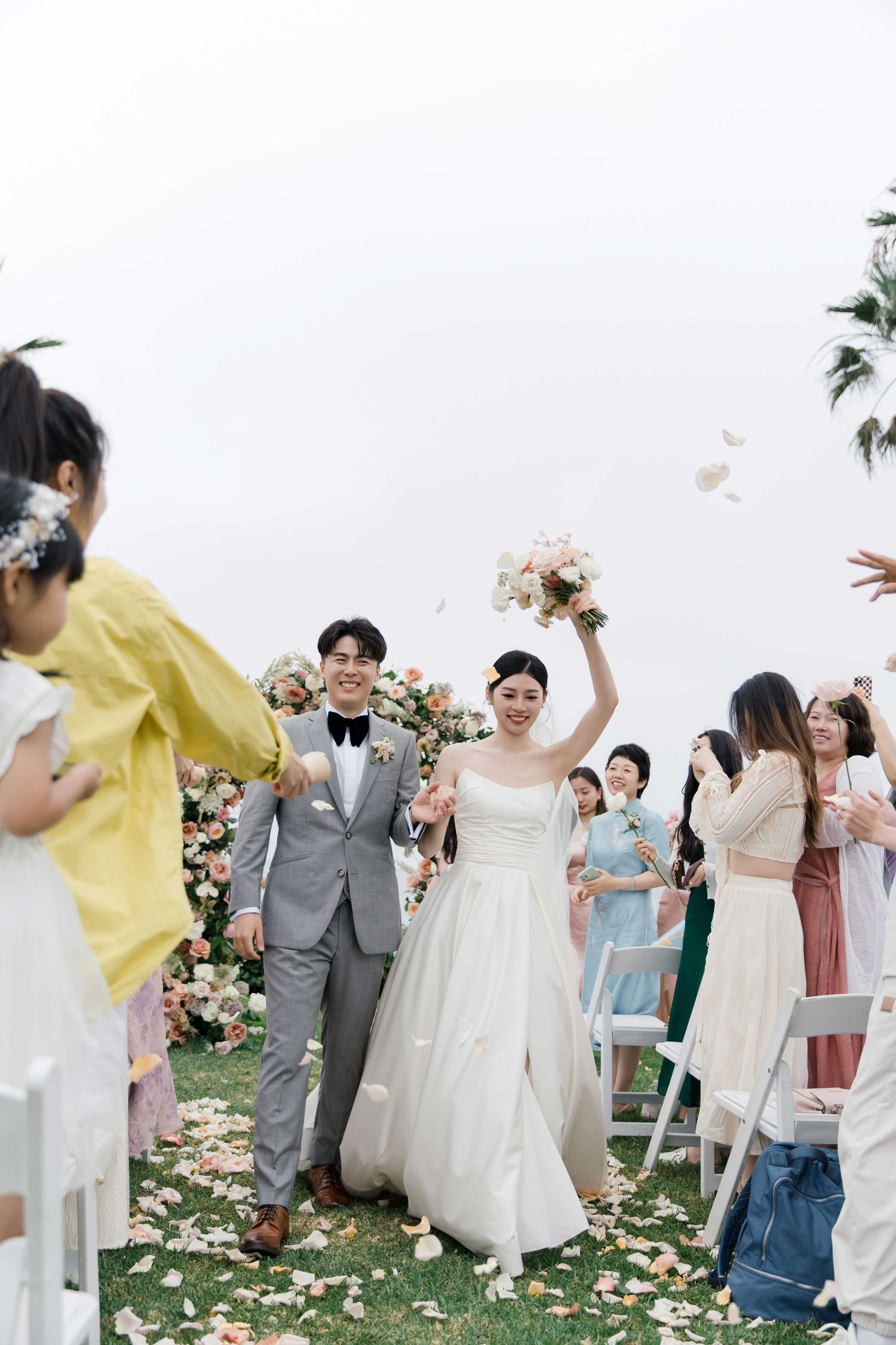 Wedding celebration with flower petals being tossed as couple walks down aisle.