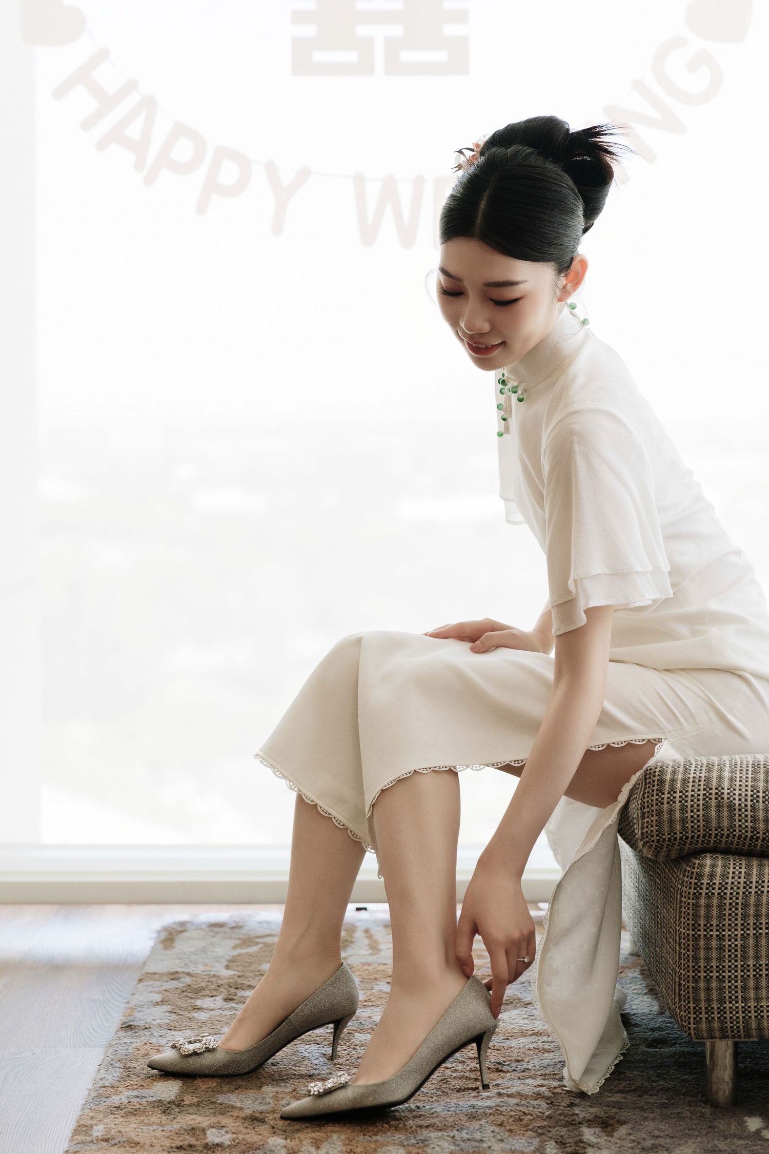 Person in white dress adjusts their shoes while sitting on a patterned couch.