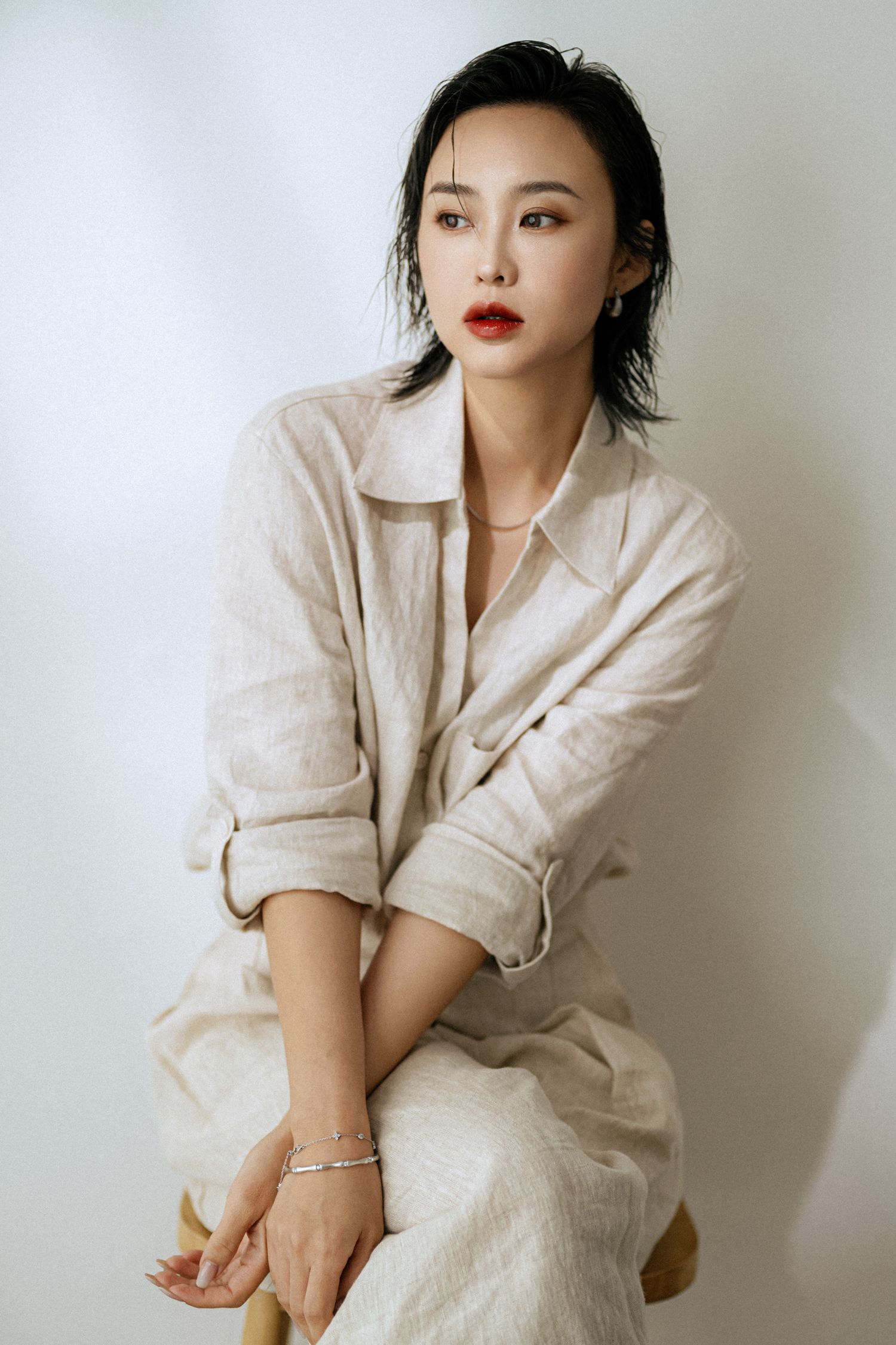 Elegant fashion portrait in cream linen outfit with statement red lips against white background.