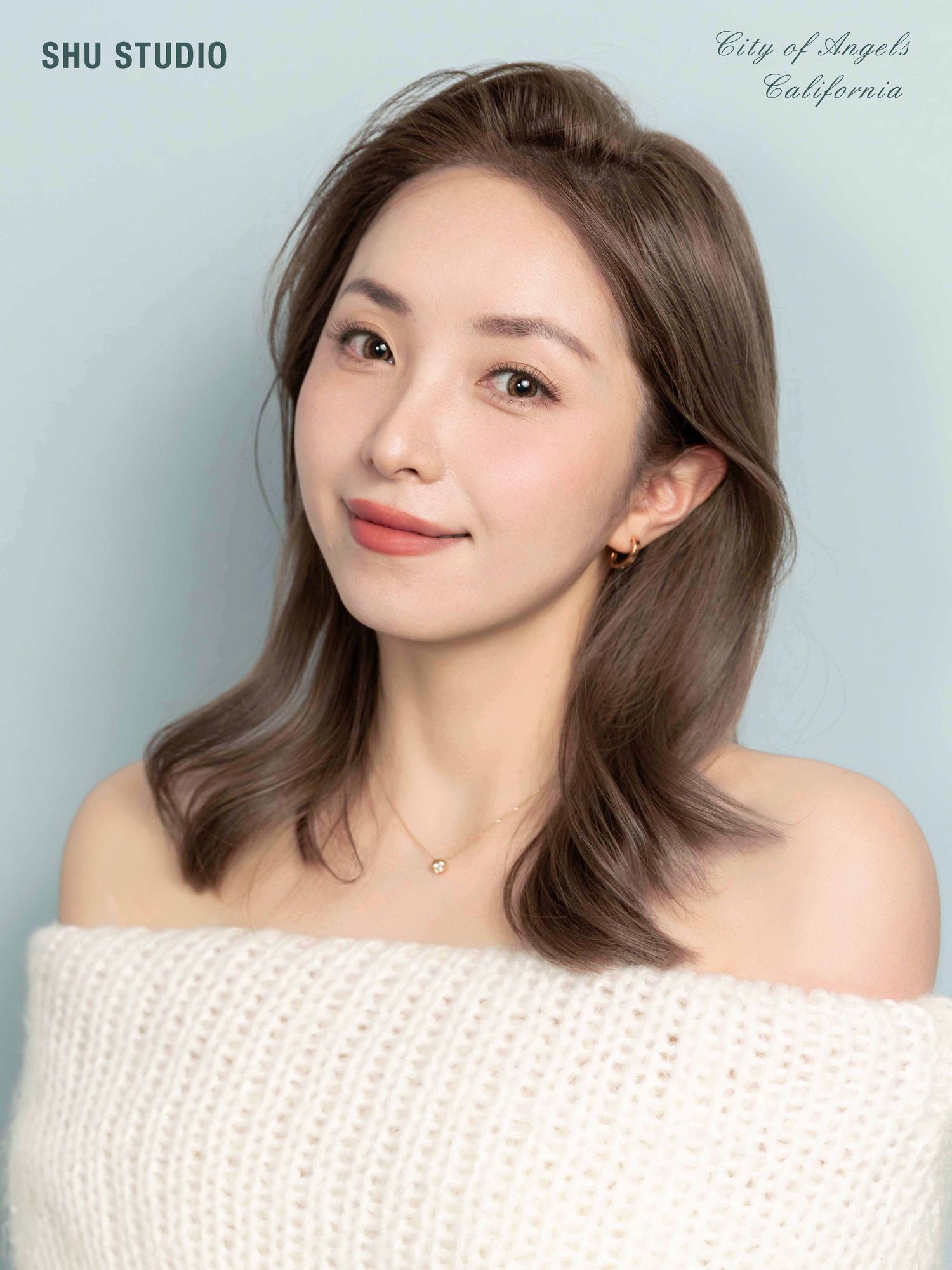 Studio portrait with off-shoulder white sweater against light blue background.
