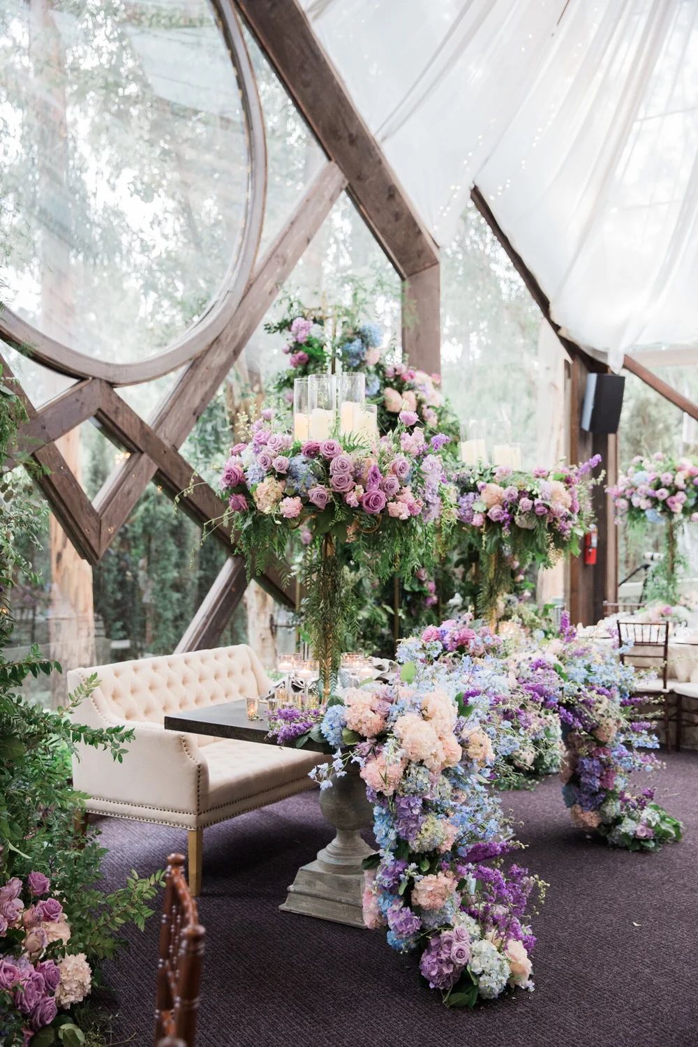 Luxurious wedding lounge area decorated with pink and purple floral arrangements under a draped tent.