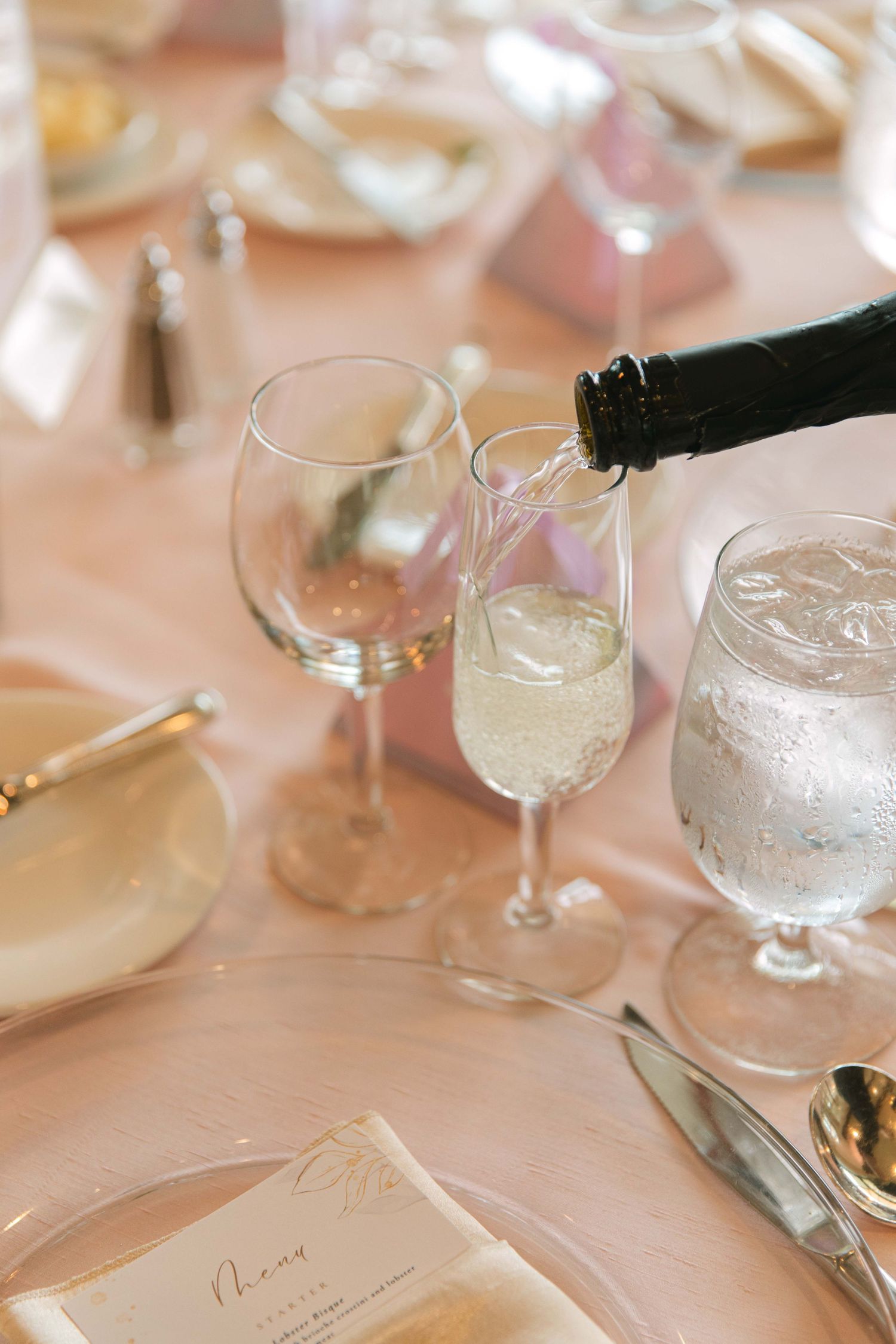 Table setting with wine glasses and place cards on pink linen tablecloth.