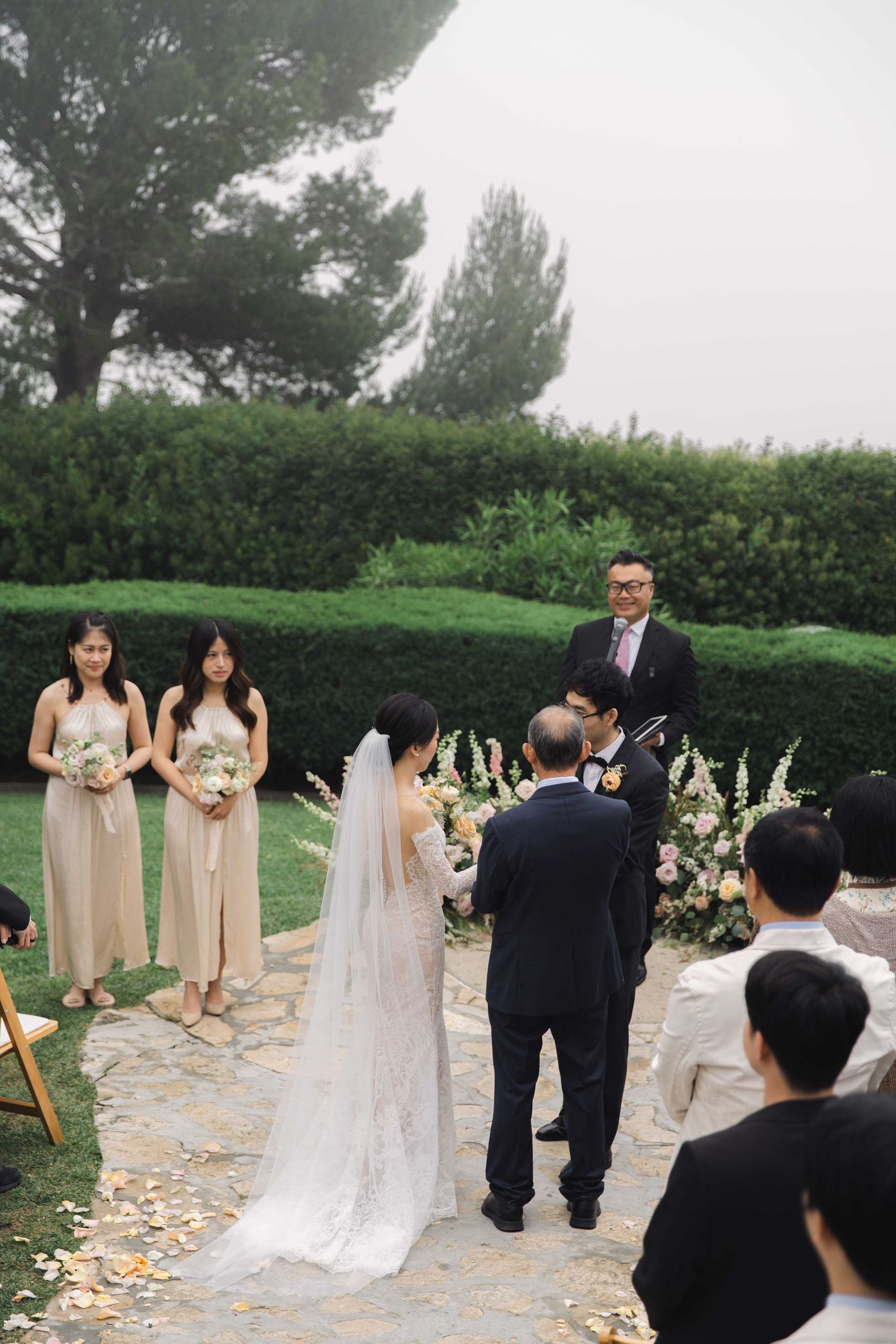 An outdoor wedding ceremony with bridesmaids in champagne dresses and floral arrangements.
