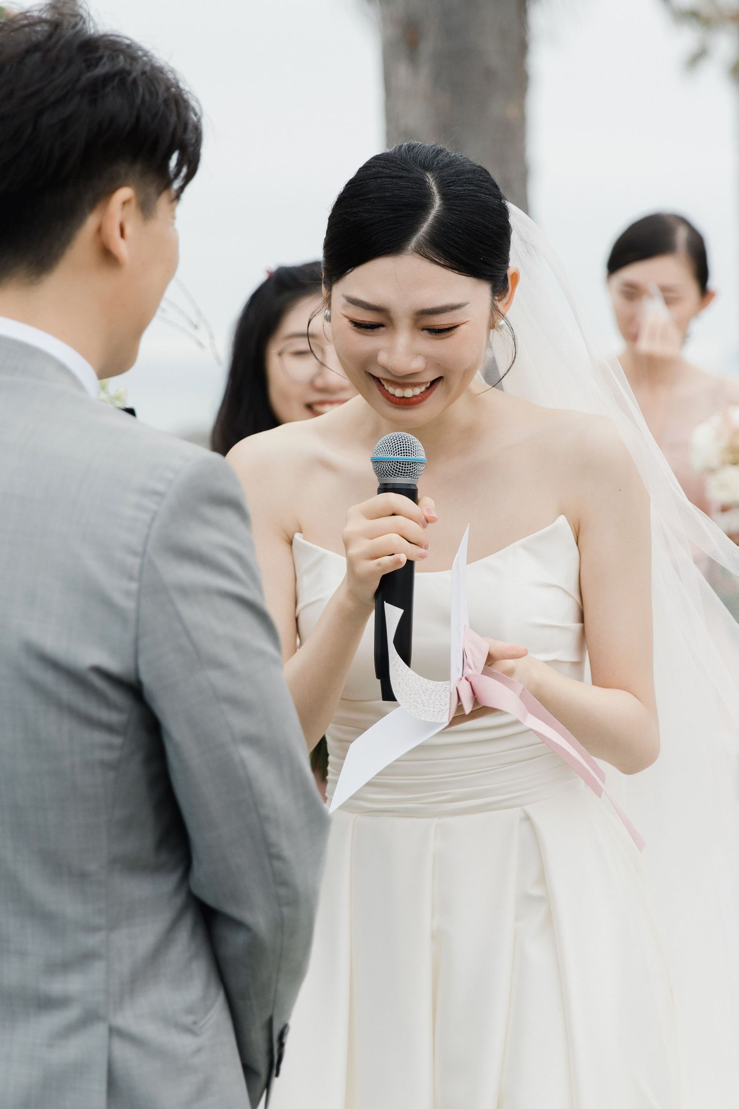 Bride in white dress reads vows during outdoor wedding ceremony.