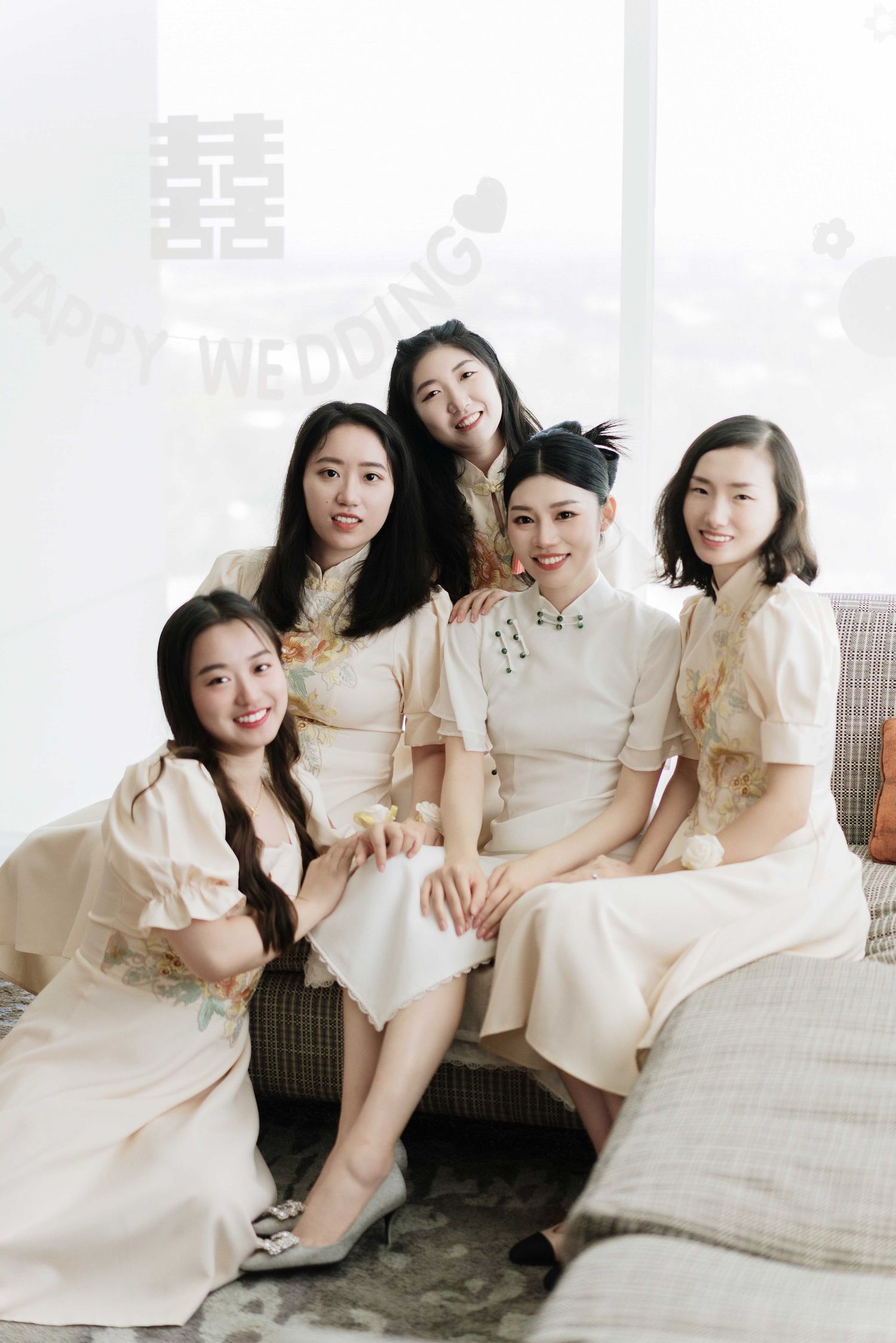 Group photo of bridesmaids in matching white traditional Chinese dresses sitting together on couch.