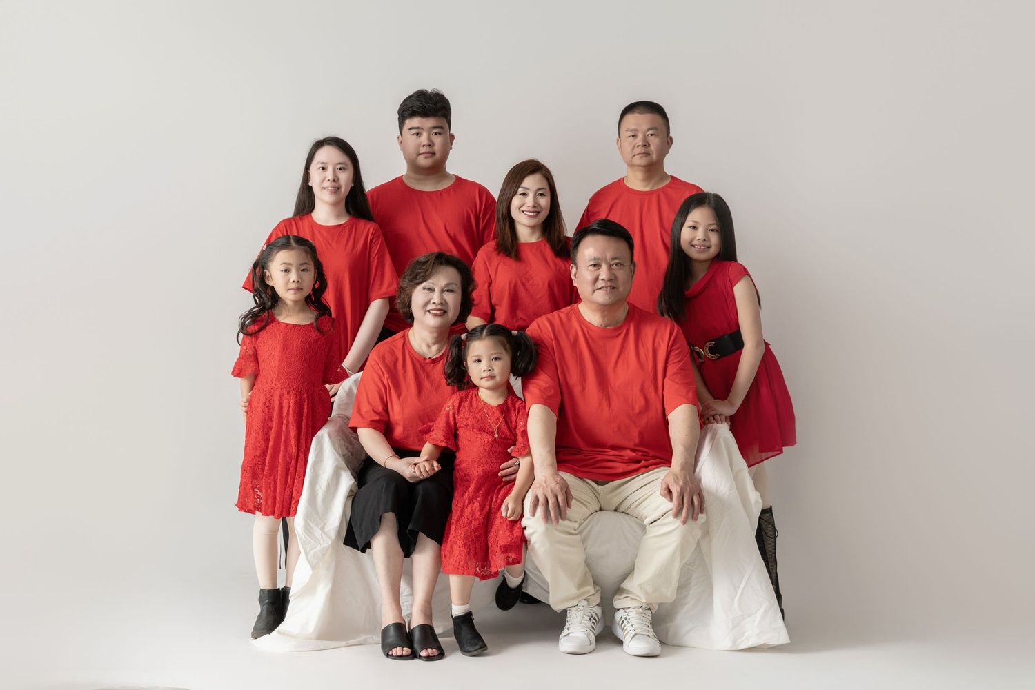 Family wearing matching red outfits poses together for professional studio photos.
