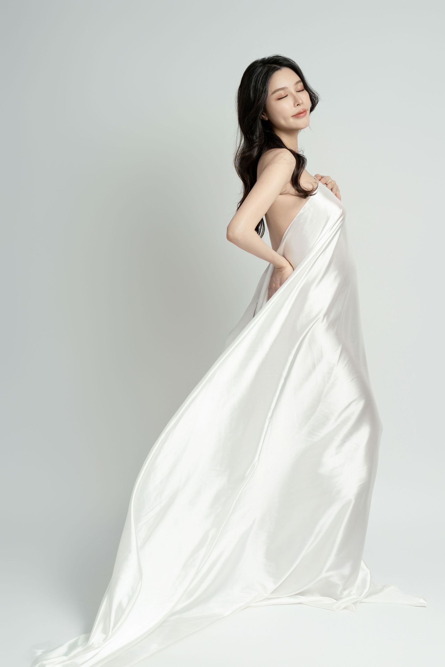 Artistic maternity photo shoot featuring flowing white fabric against light background.