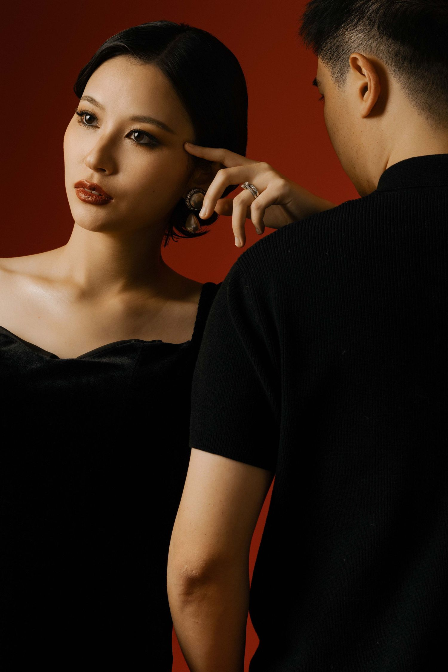 Intimate couple photoshoot featuring black outfits against dark red background.