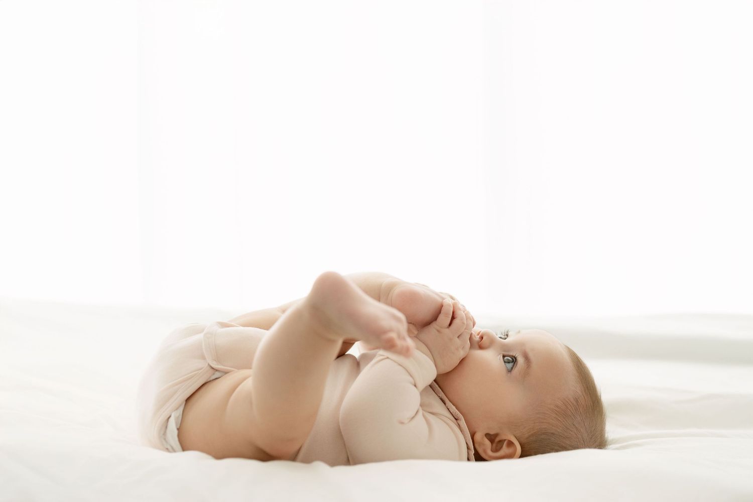 Baby resting peacefully on white sheets in soft lighting.