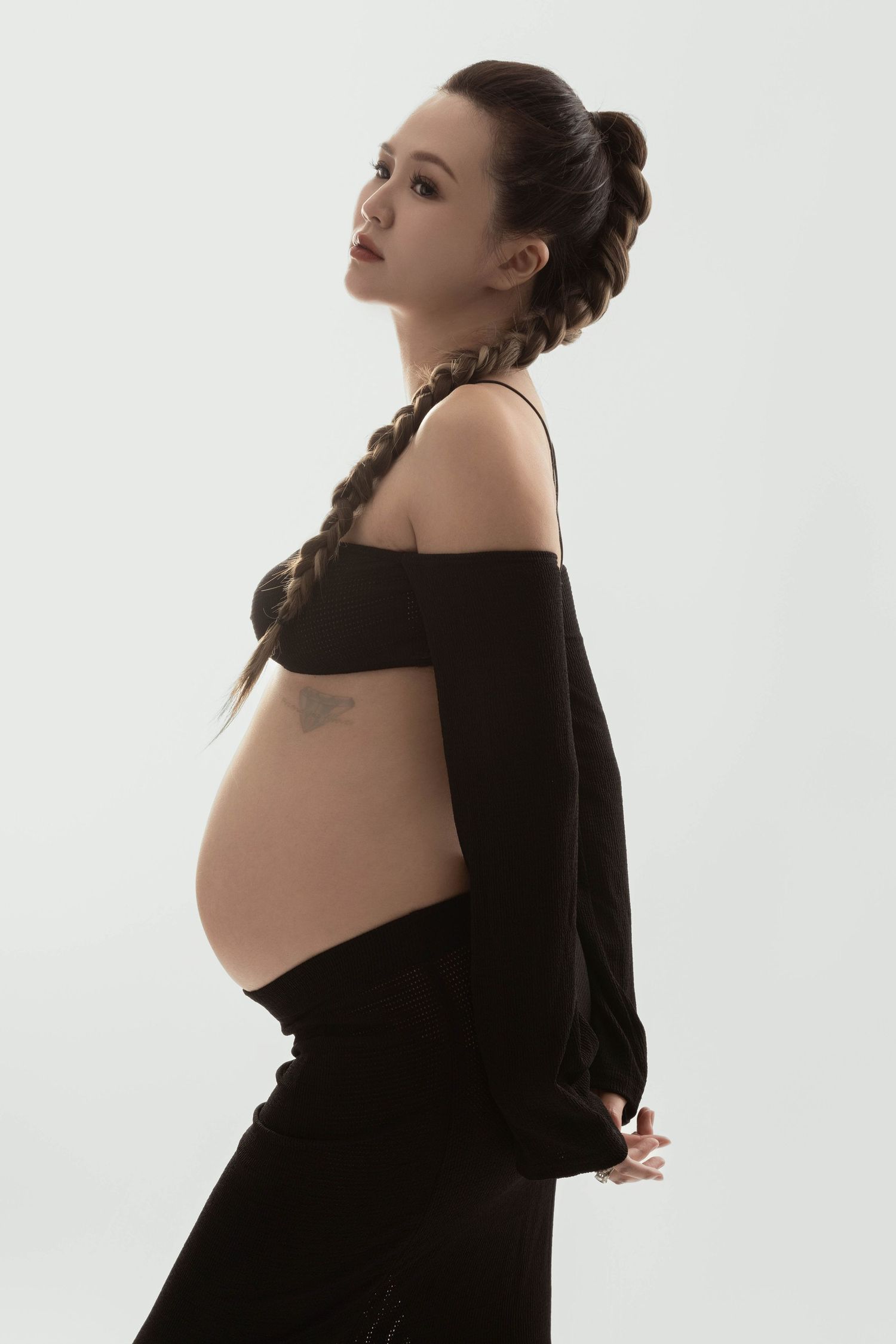Elegant maternity photoshoot with figure in black dress against white background.