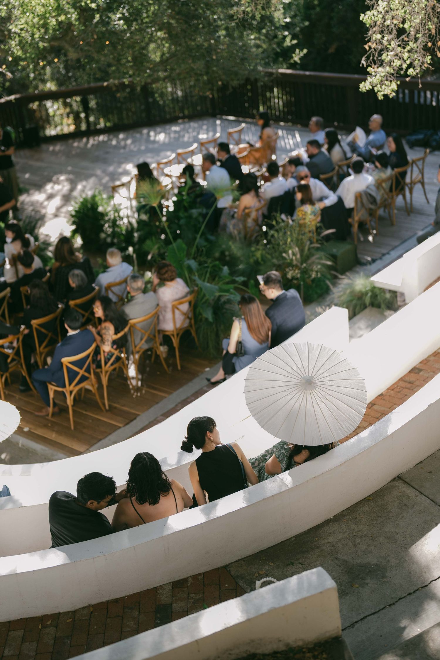 Guests seated at outdoor wedding ceremony with white parasol and curved seating arrangement.
