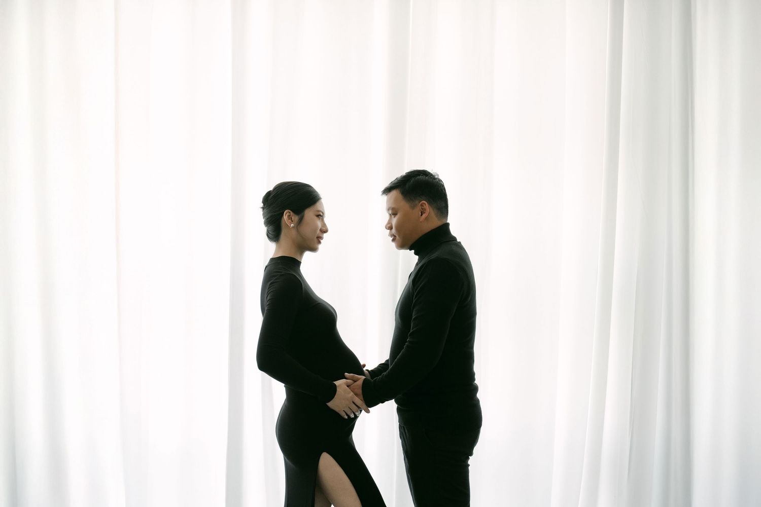 Intimate couple maternity photos against white curtain background.