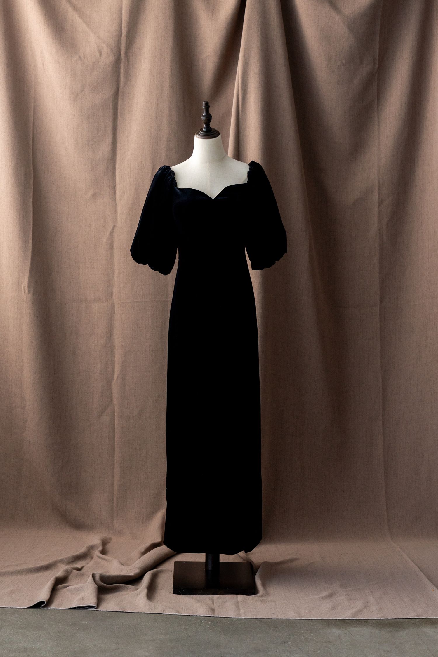 Black formal dress displayed on mannequin against brown backdrop from various angles.