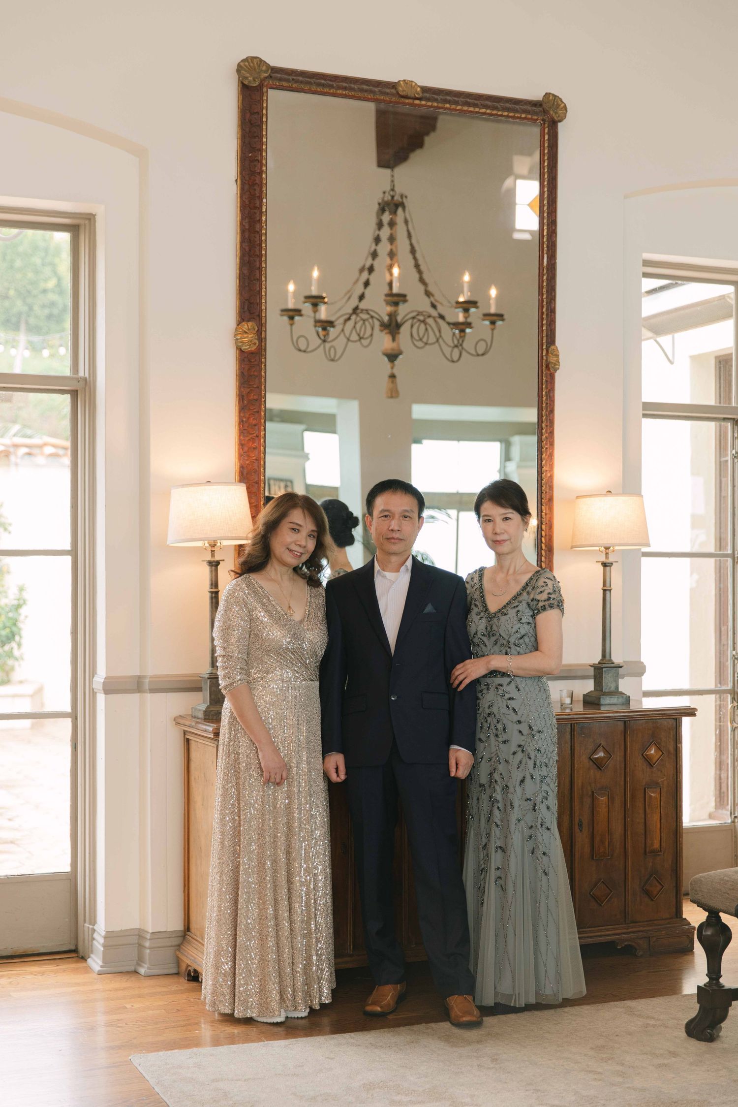 A wedding party poses in an elegant room with a large mirror and chandelier.