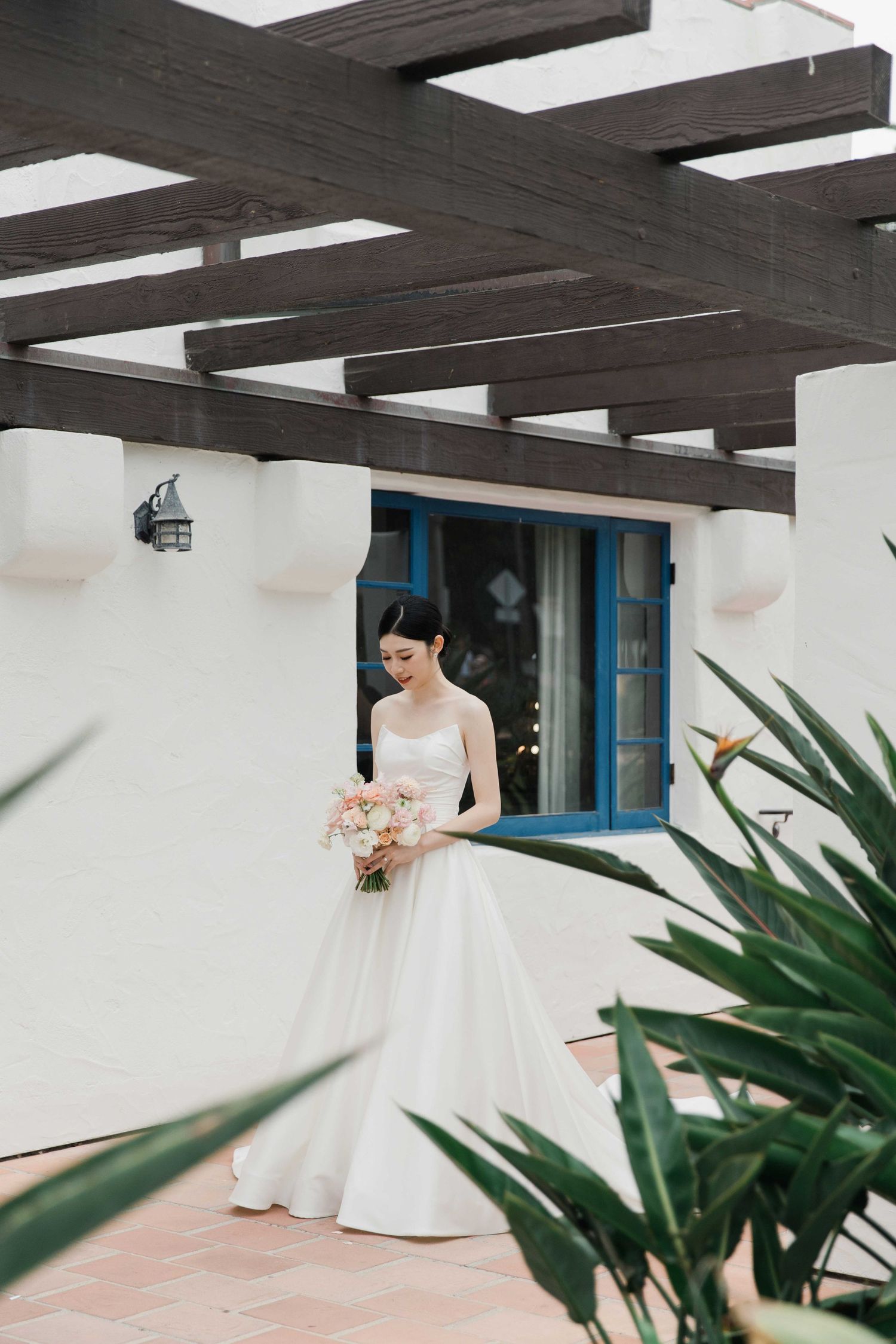 Elegant white wedding dress photographed against modern architecture with tropical plants.