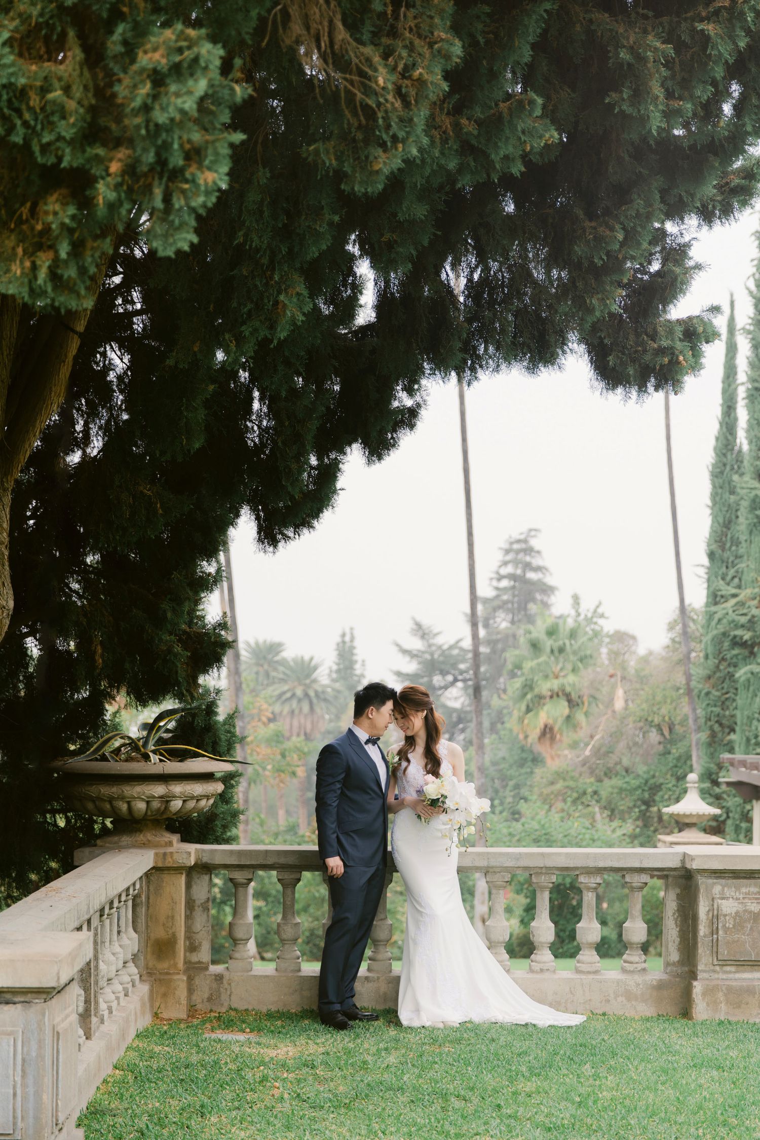 A romantic wedding moment captured in a garden setting with stone balustrades and cypress trees.