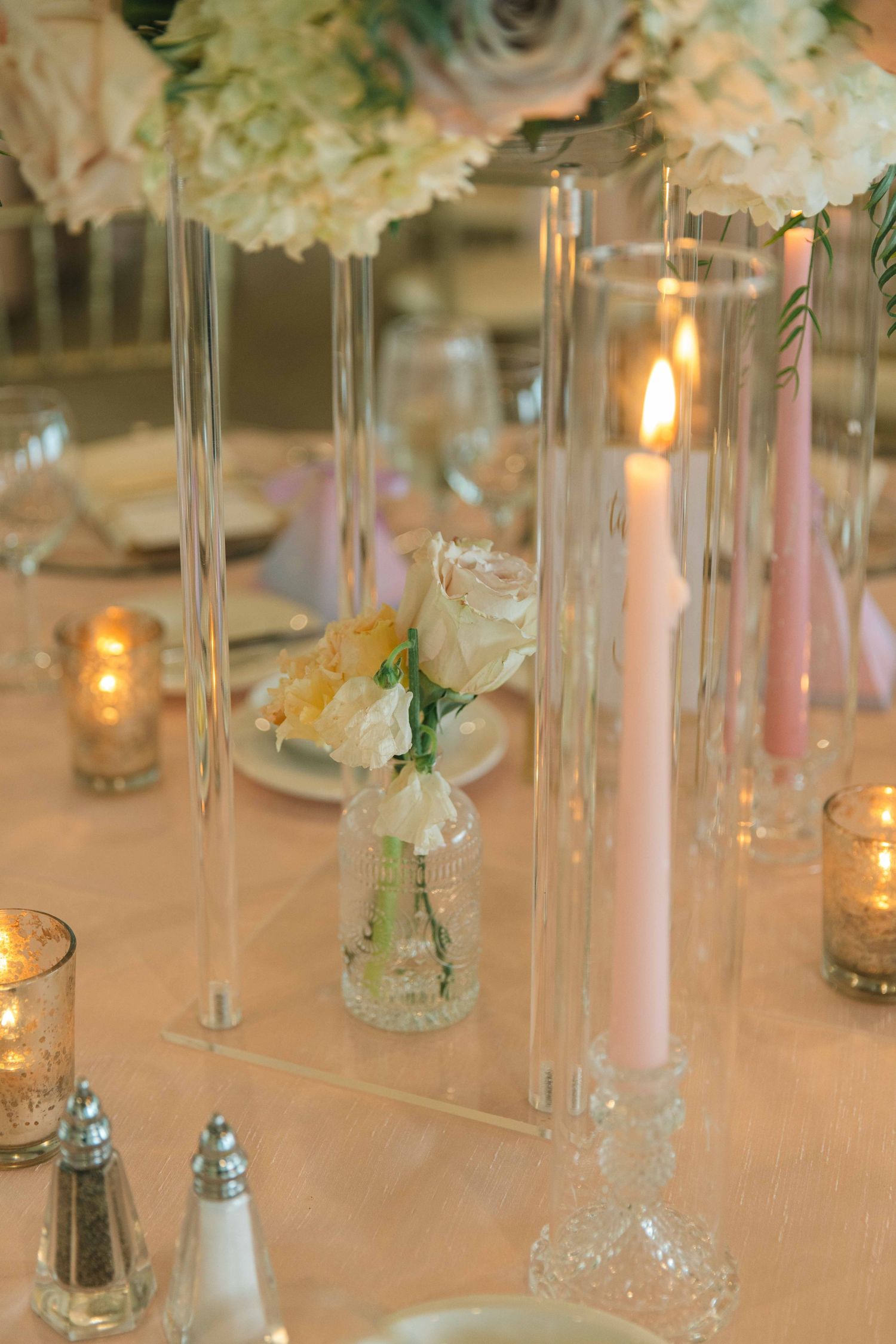 Elegant wedding reception table with glass vases, candles, and soft pink floral centerpieces.