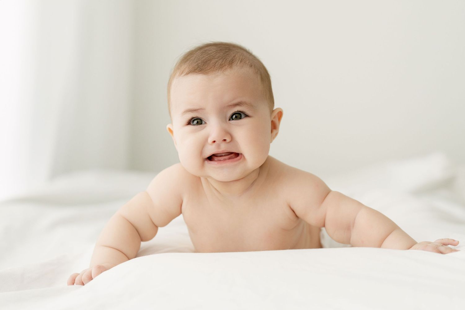 Sweet baby lying on white bedding with a gentle smile and soft lighting.