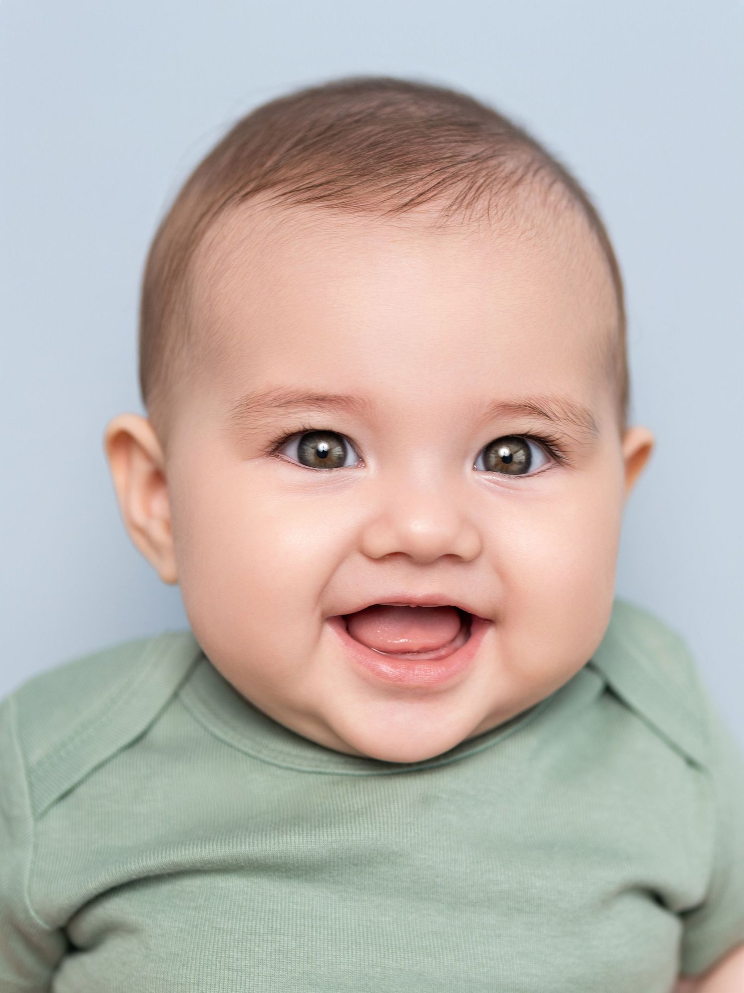 Happy infant wearing light green outfit against soft blue backdrop.