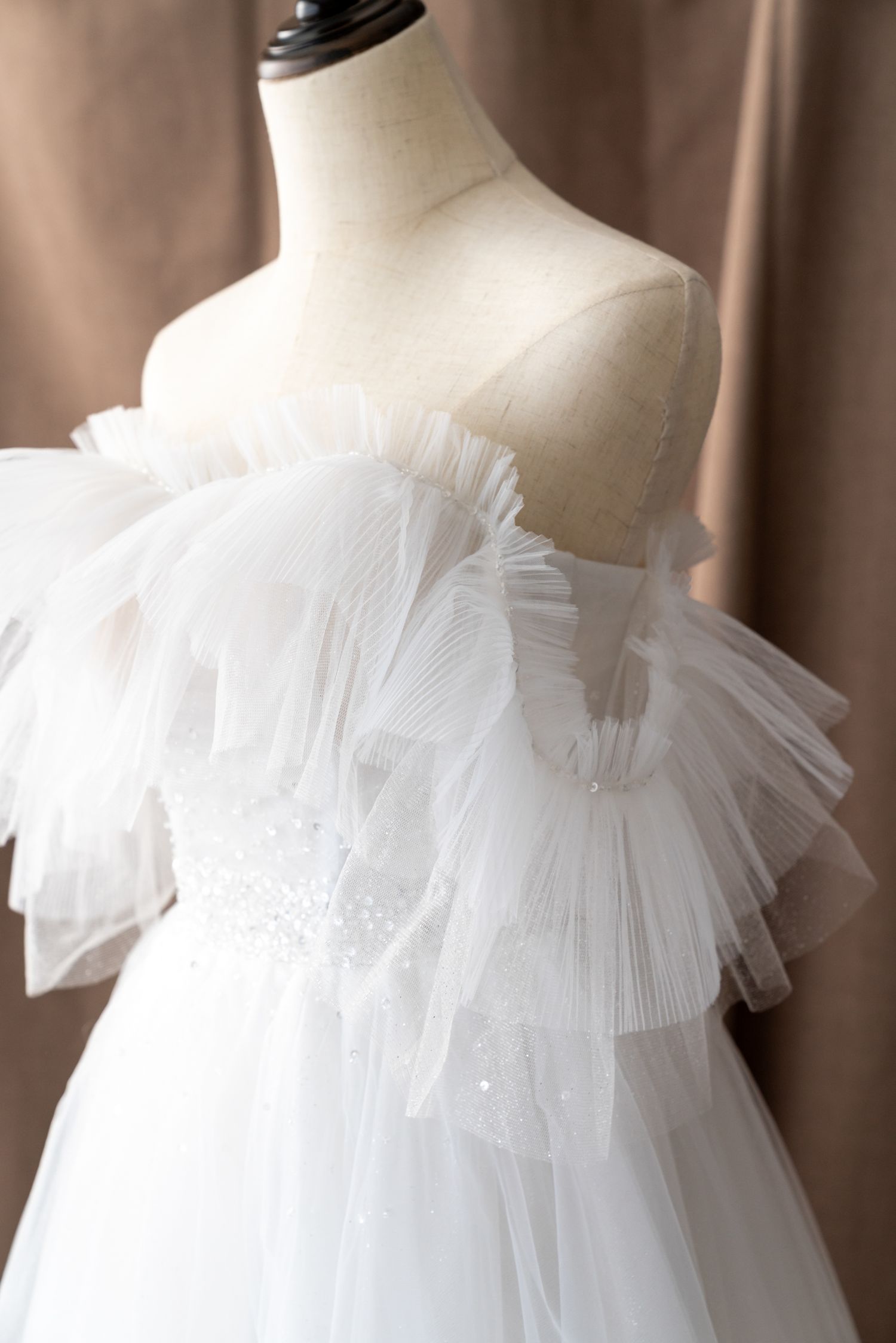 White tulle ruffled neckline detail of a wedding dress on mannequin.