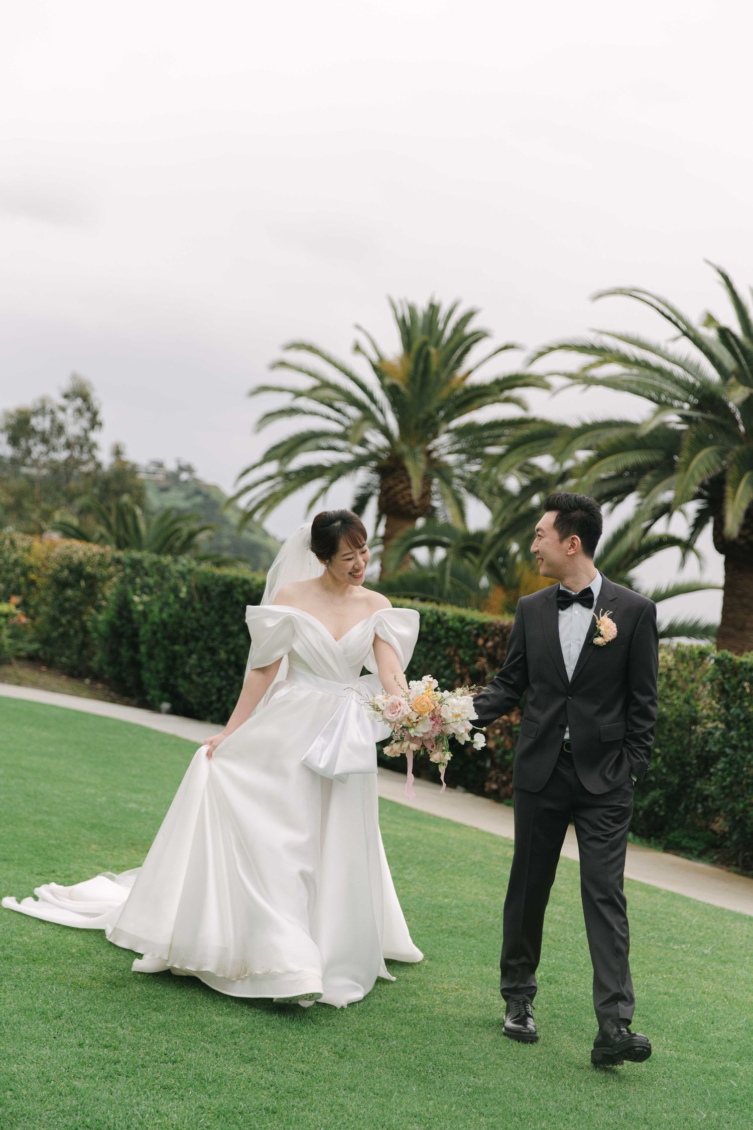 Couple sharing playful moments on grassy lawn with palm trees in background.