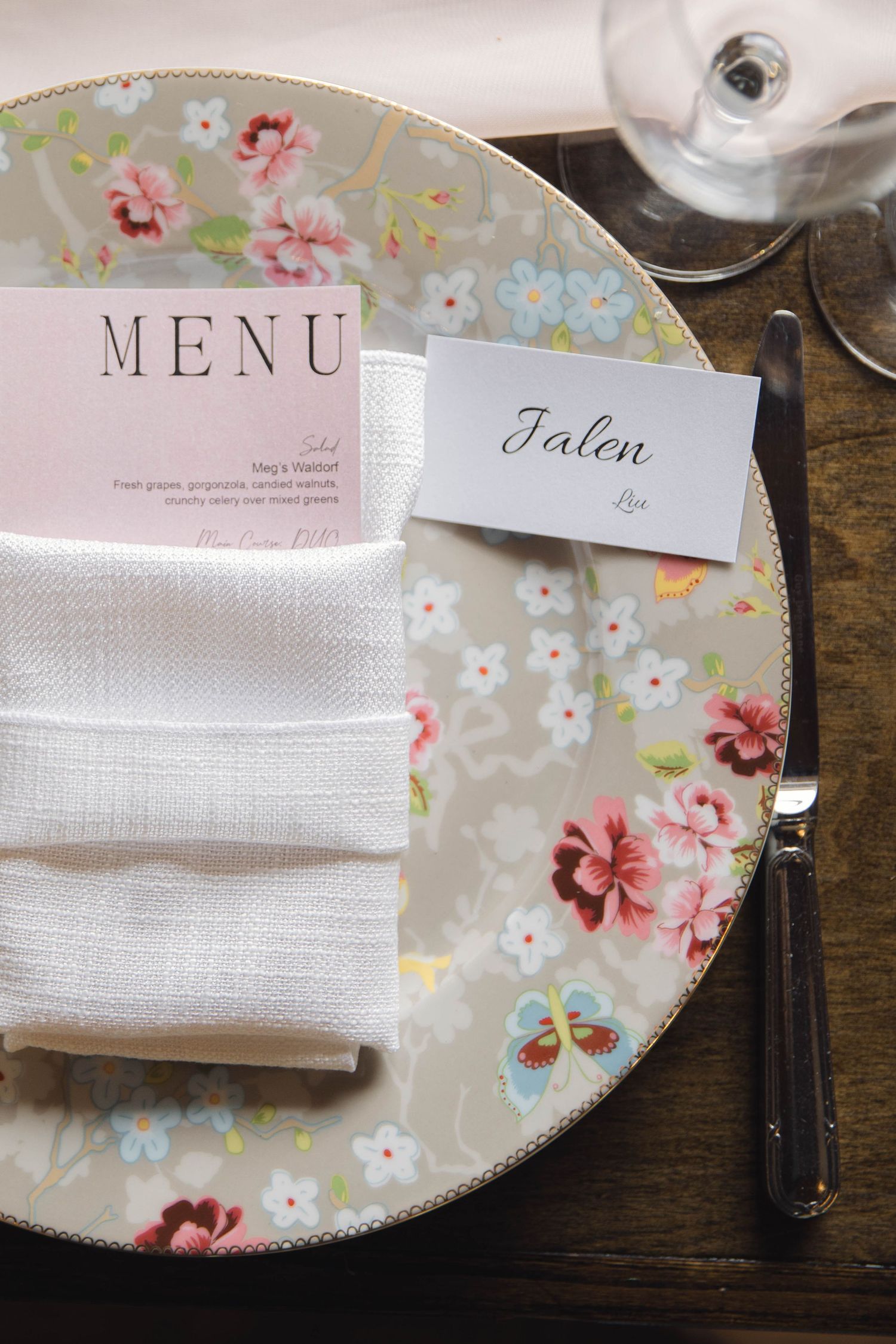 Floral patterned plate with pink menu card and white napkin at elegant place setting.