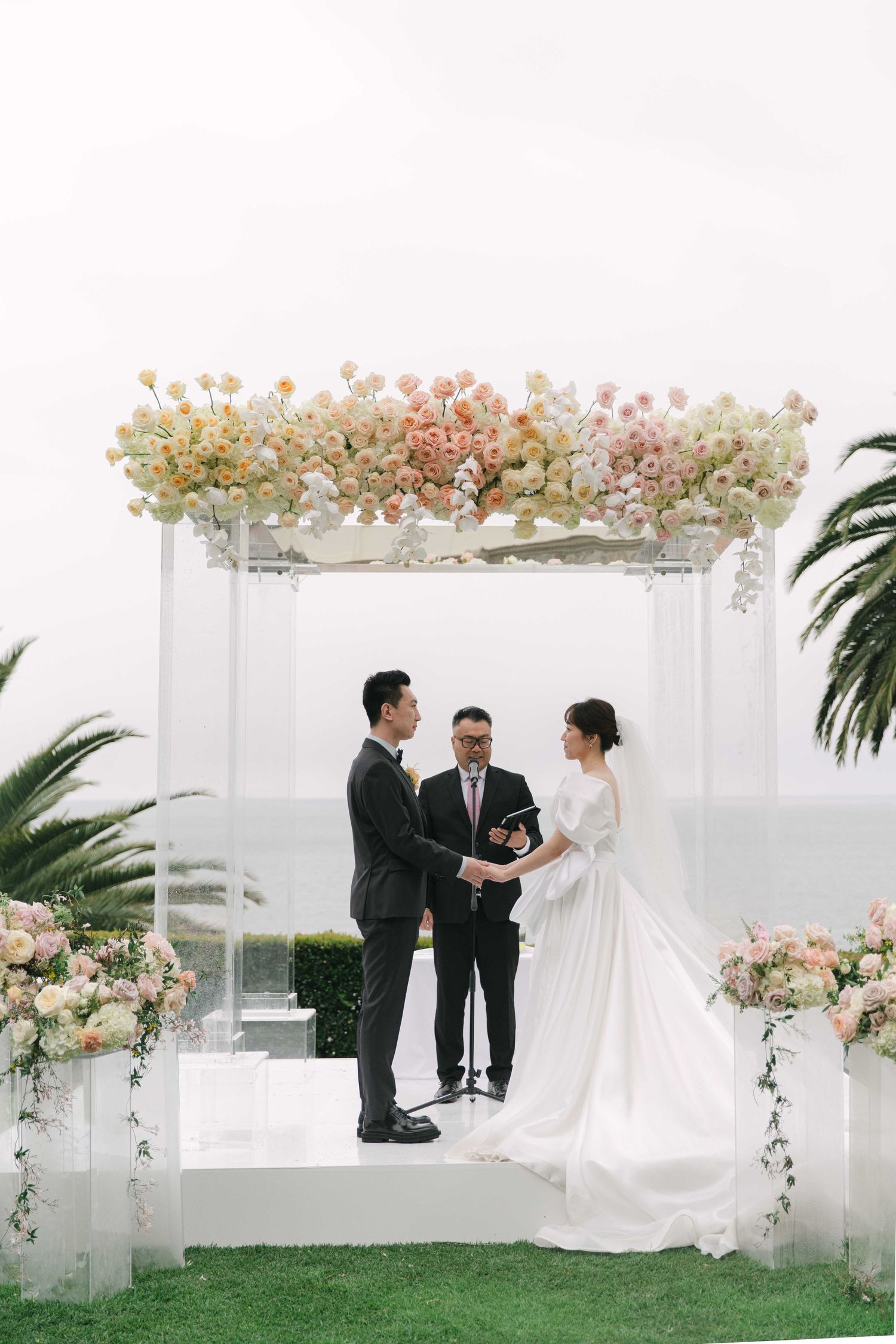 White wedding arch decorated with pink and peach flowers against a bright outdoor setting.