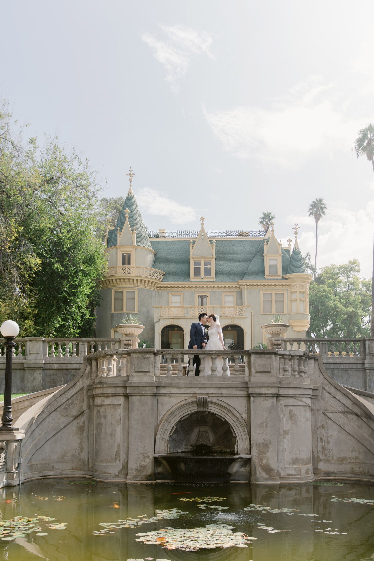 Historic mansion with ornate stone bridge and lily pond creates a romantic wedding venue backdrop.
