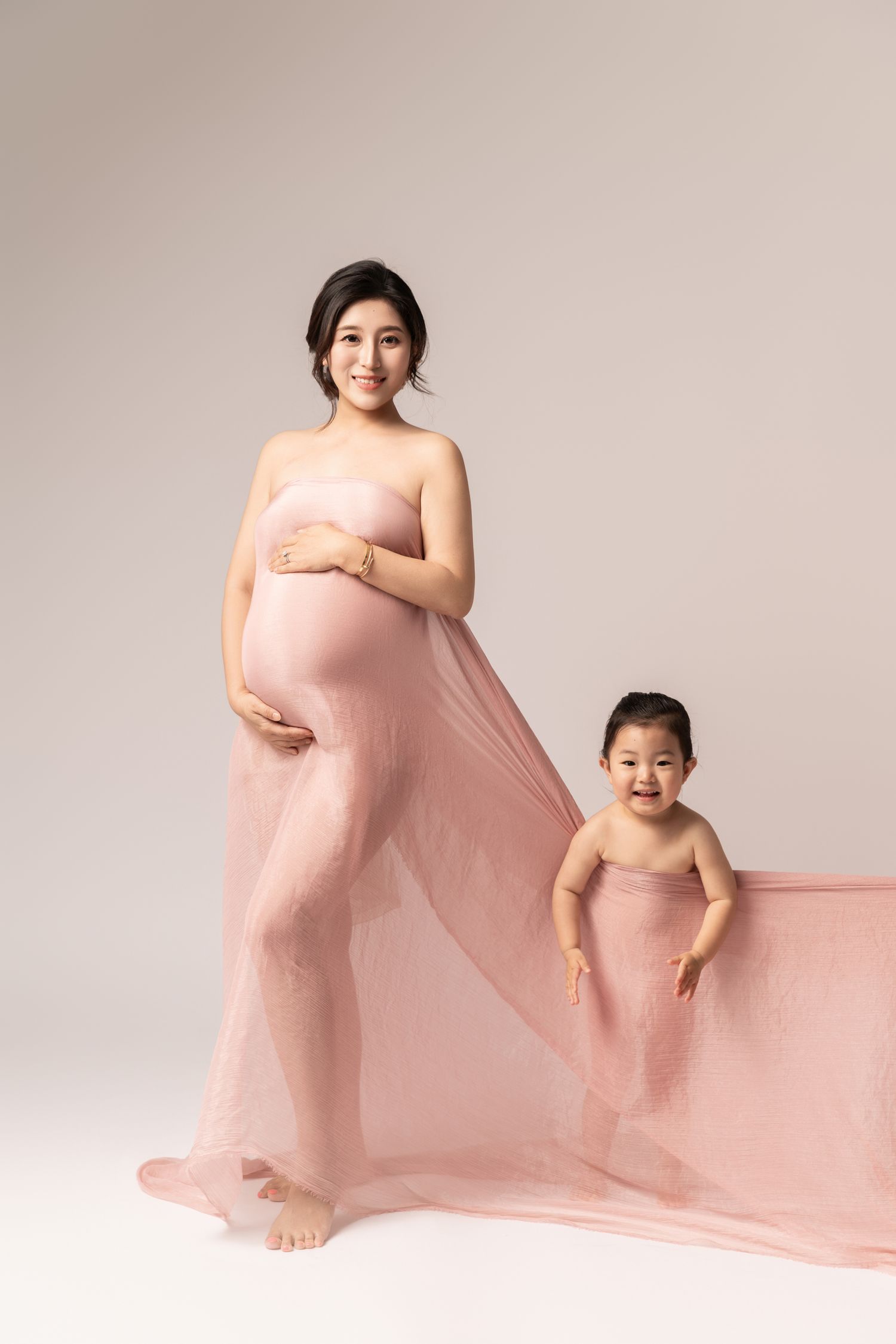 Ethereal maternity portraits with flowing pink fabric and natural lighting.