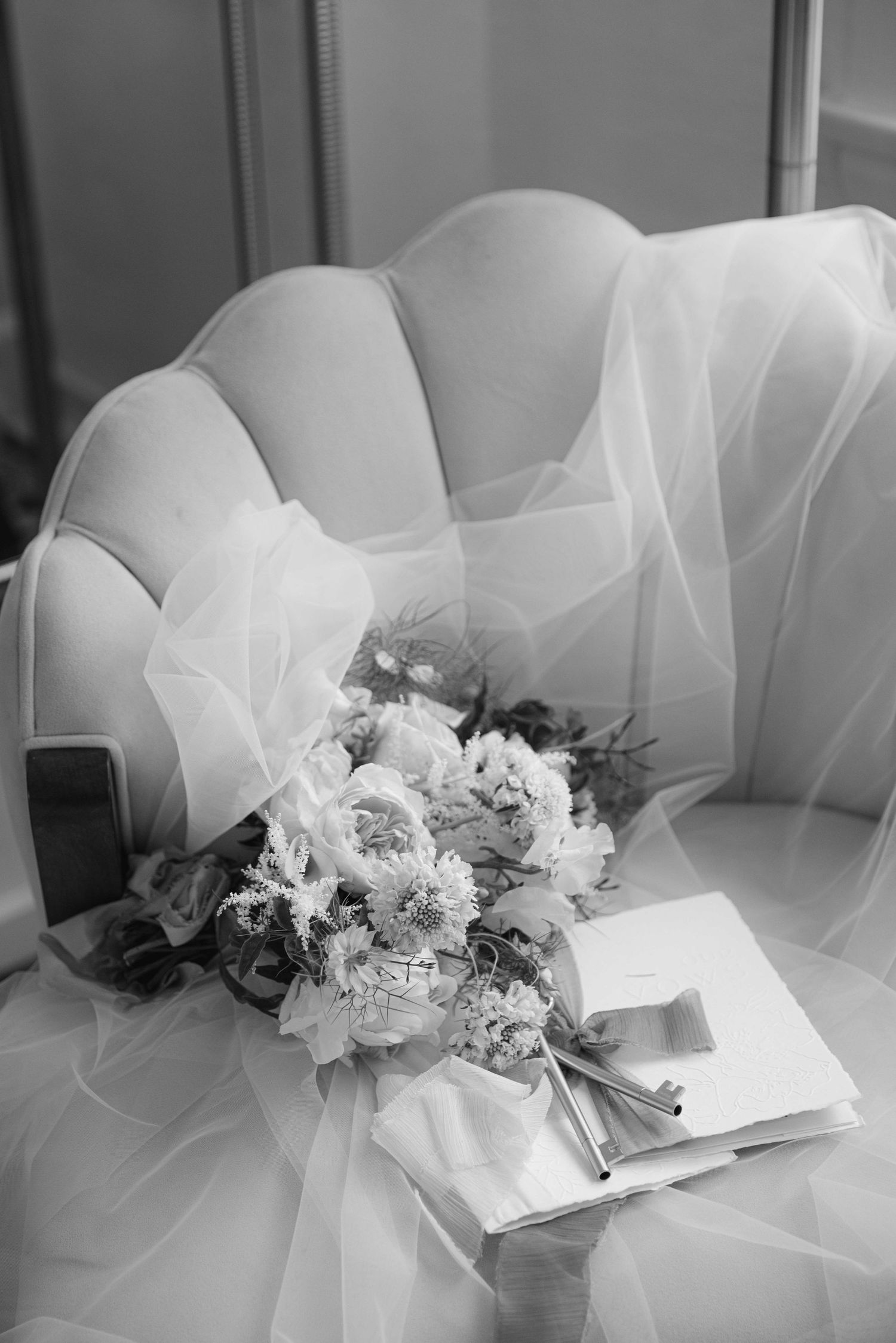 Wedding bouquet and veil arranged on white tufted chair in black and white.