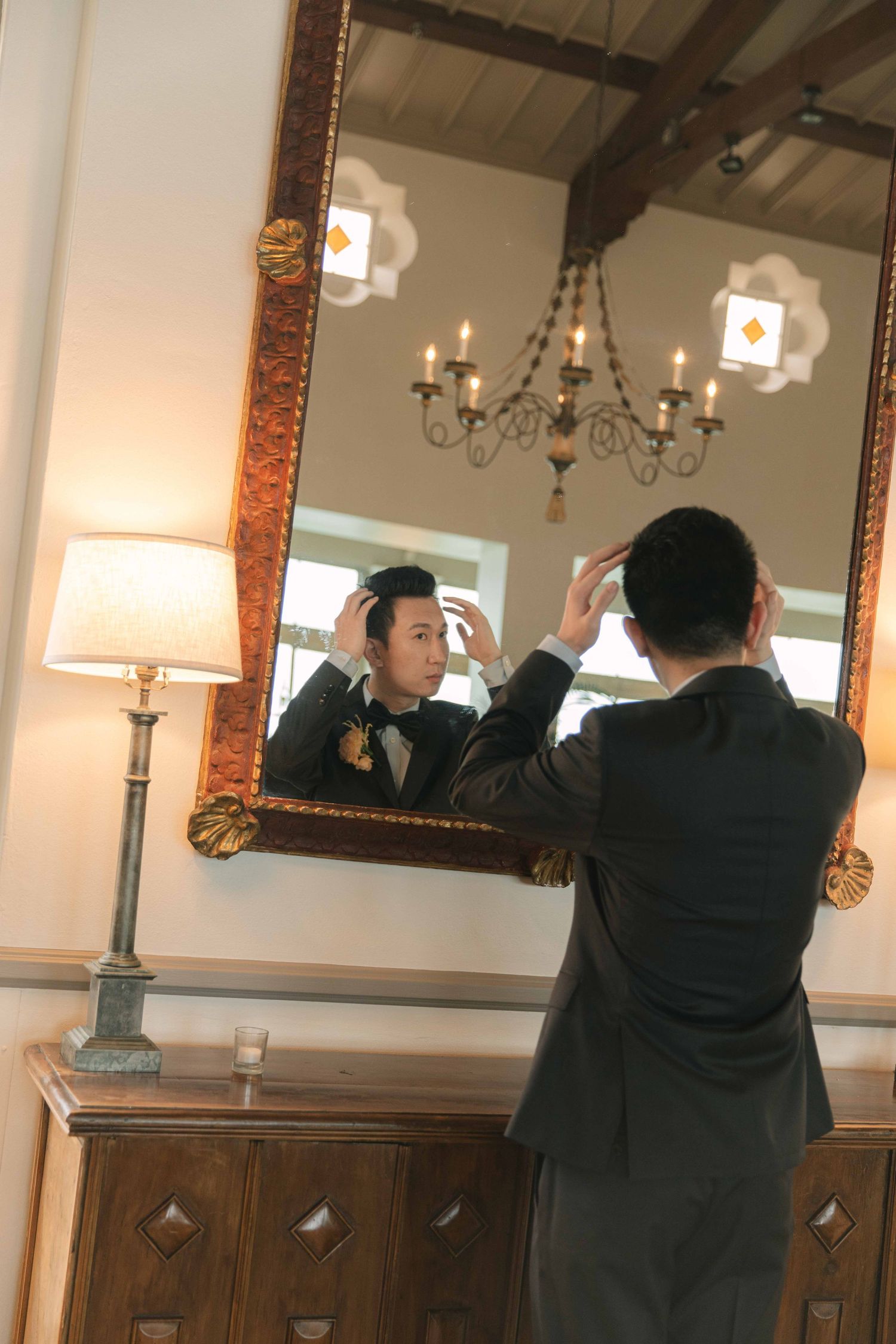 Person in formal attire adjusts their appearance in an ornate mirror.
