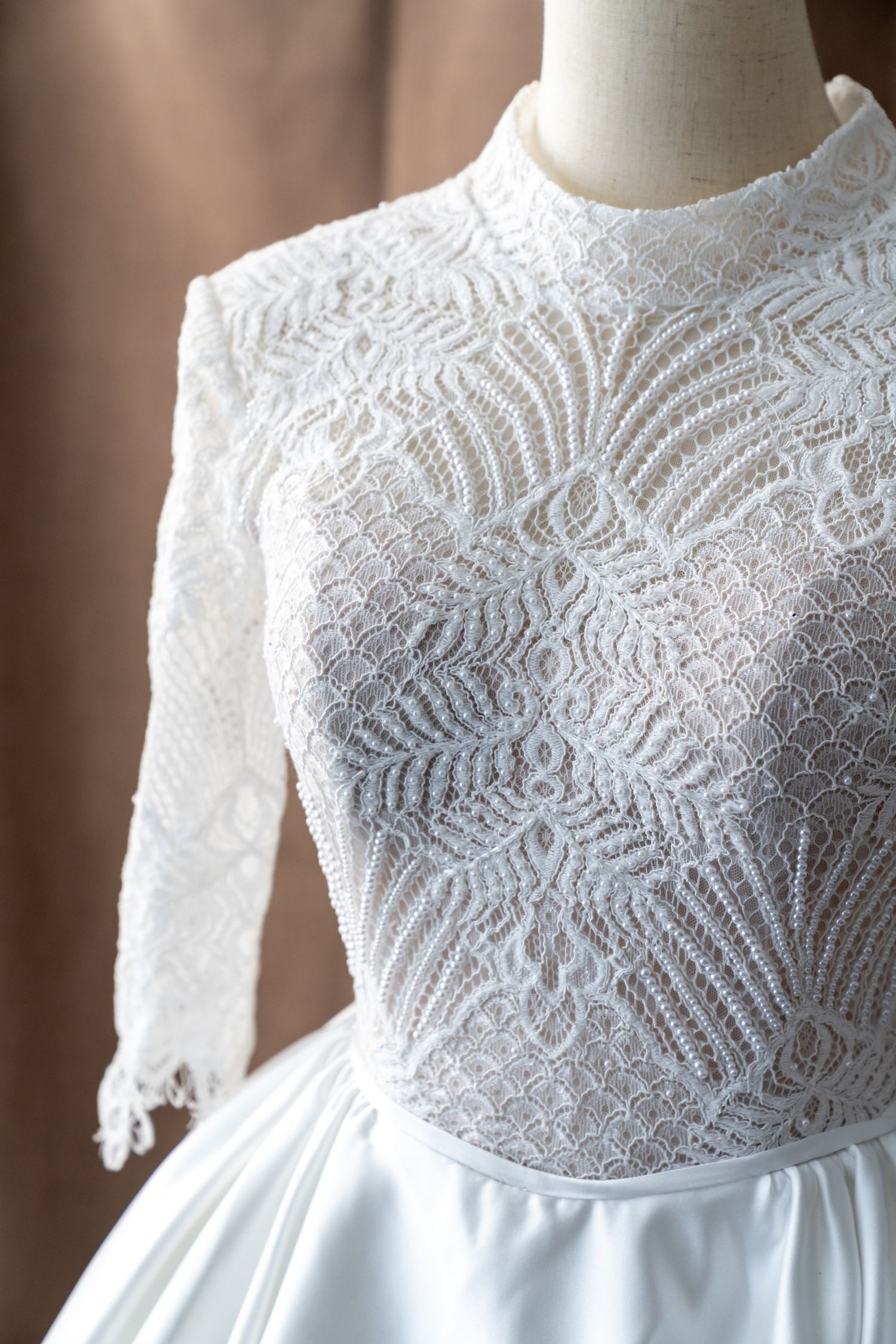 Close-up detail of white lace pattern on wedding dress bodice with delicate beadwork.